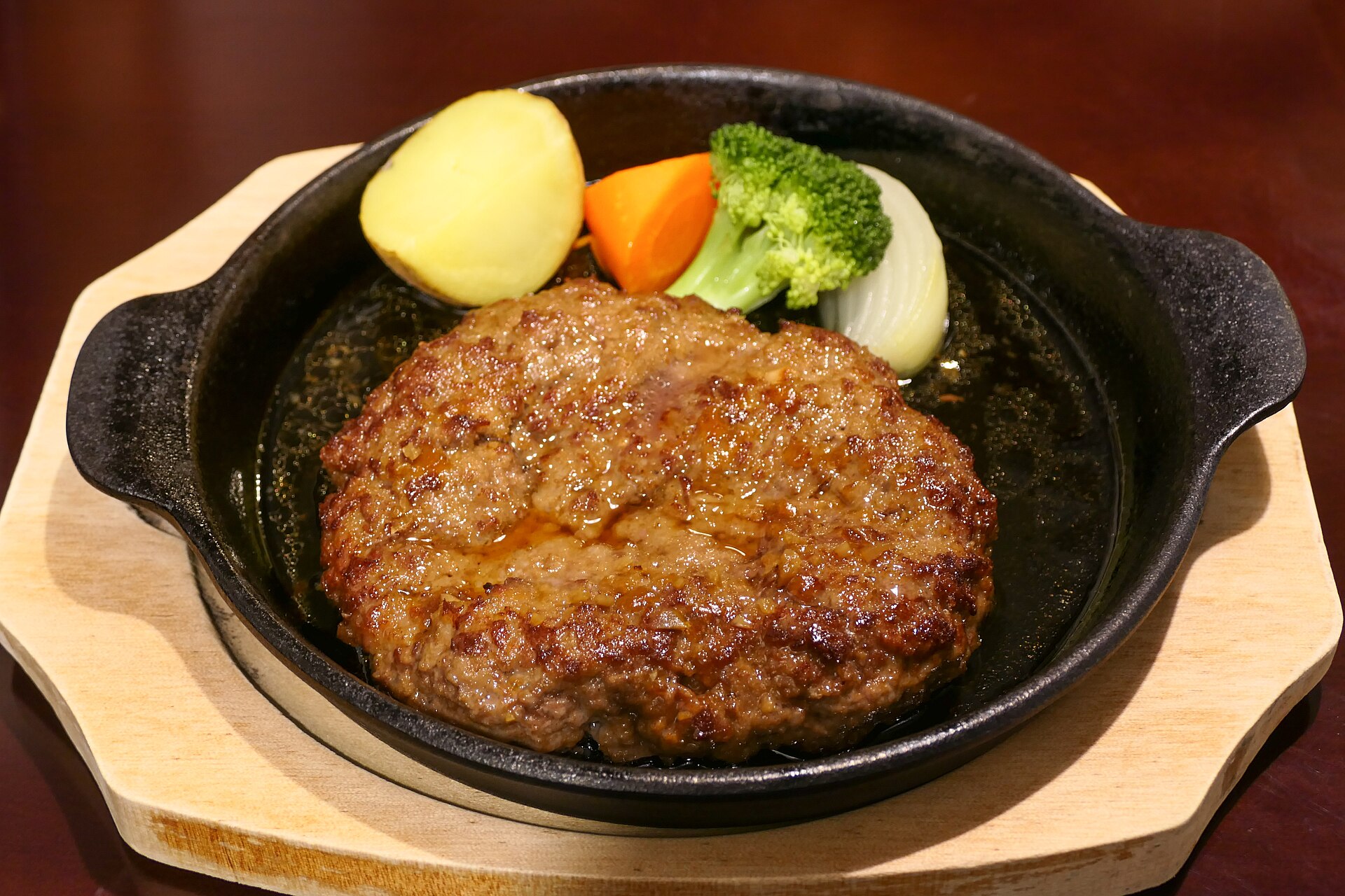 Hamburger steak on a hot iron plate with potato, carrot and broccoli