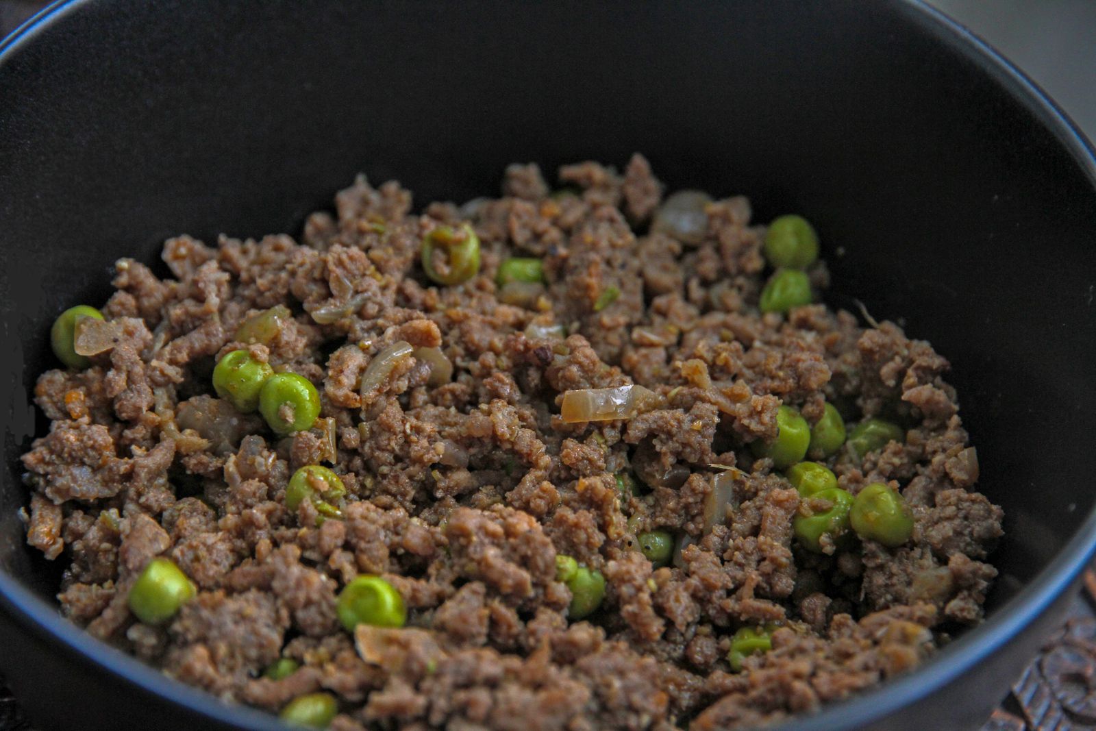 Browned ground meat with green peas and onion in a pan