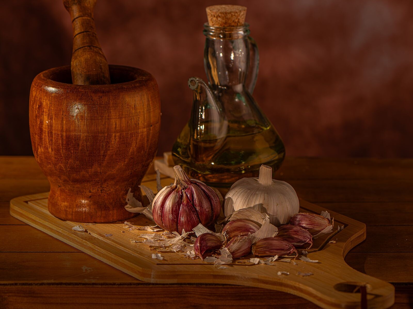 Garlic bulbs, olive oil and a mortar on a rustic table