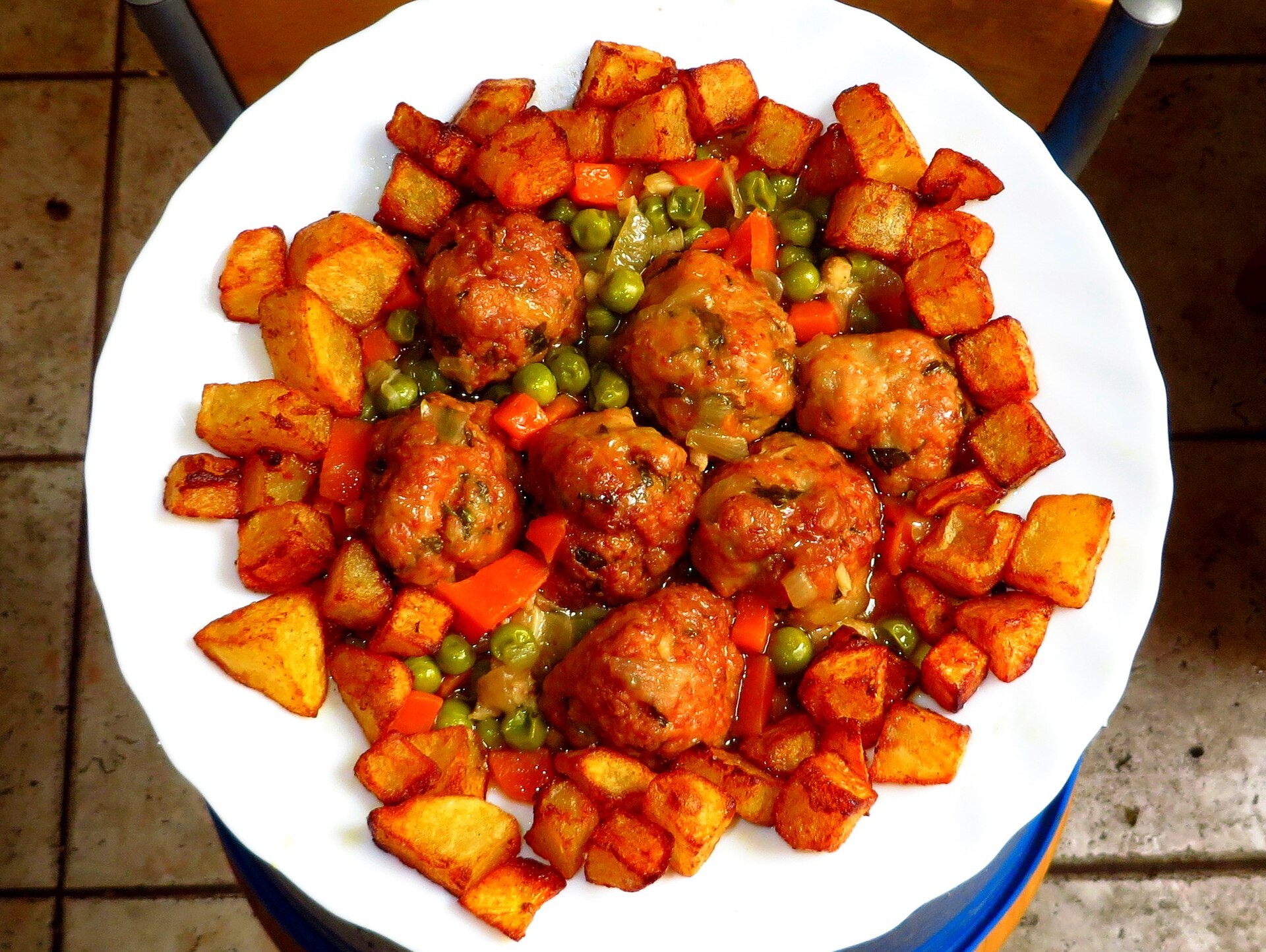 Spanish meatballs in tomato sauce with fried potatoes and peas