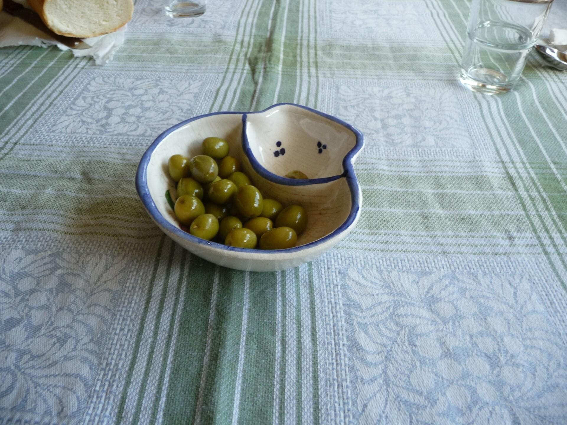 Small bowl of marinated green olives on a striped tablecloth