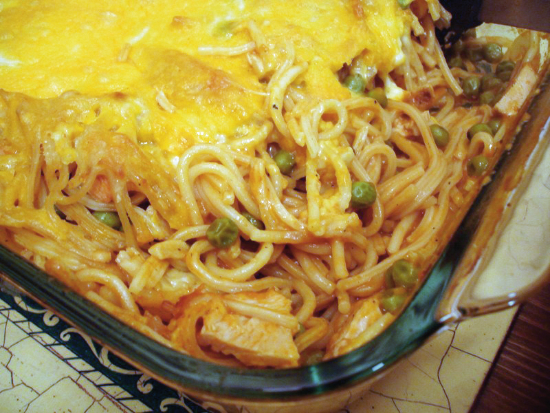 Turkey Tetrazzini with peas and melted cheese in a glass baking dish, a classic among Tetrazzini recipes