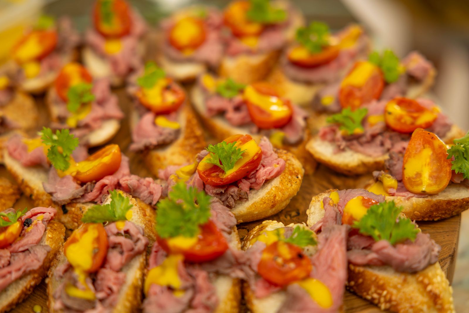 Rows of roast beef crostini with orange tomato and herbs