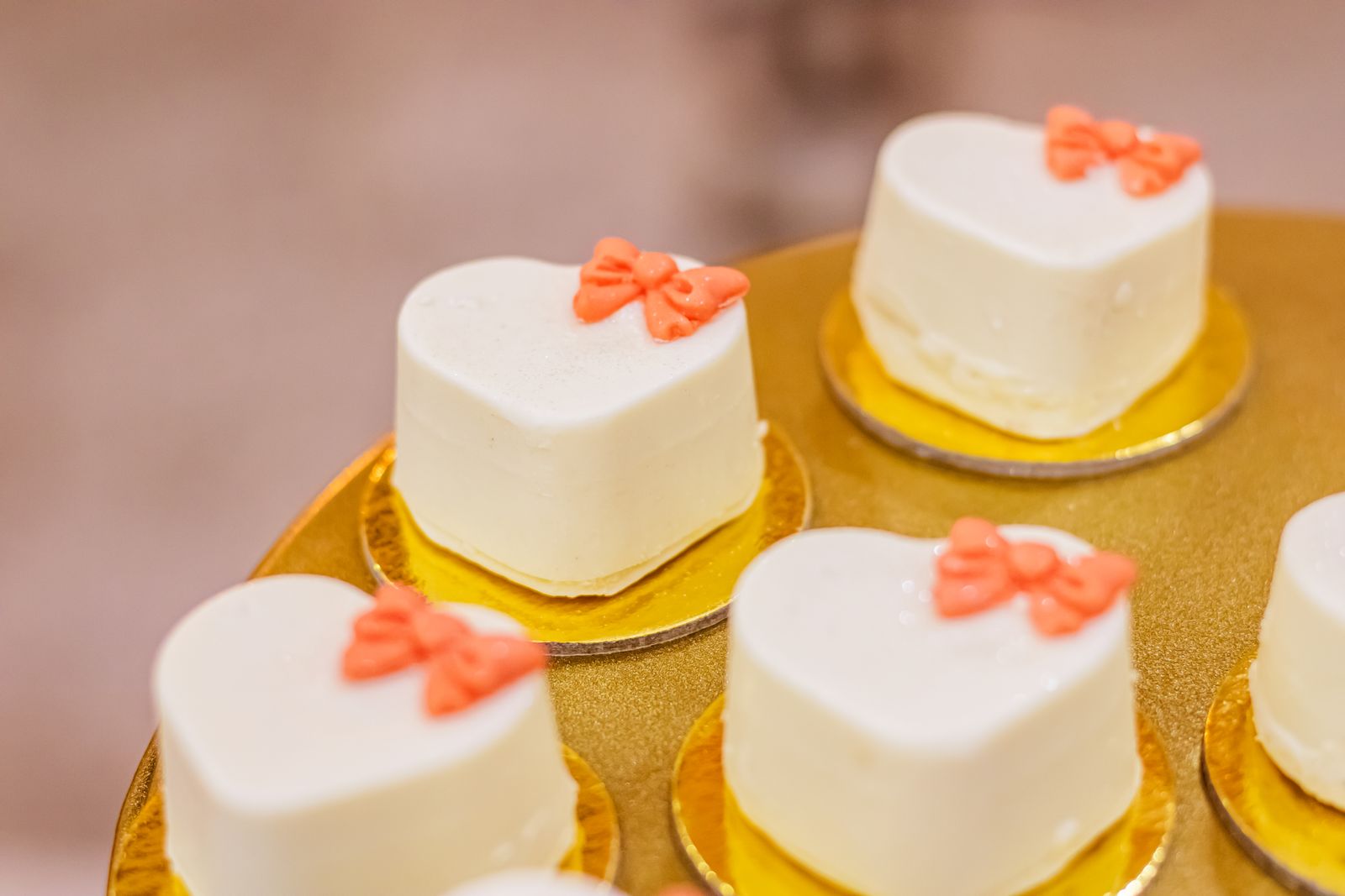 Little white frosted tea cakes with pink bows on gold boards