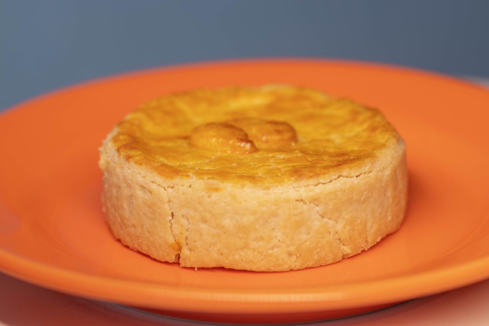 Mini pork pie with golden hot water crust on an orange plate