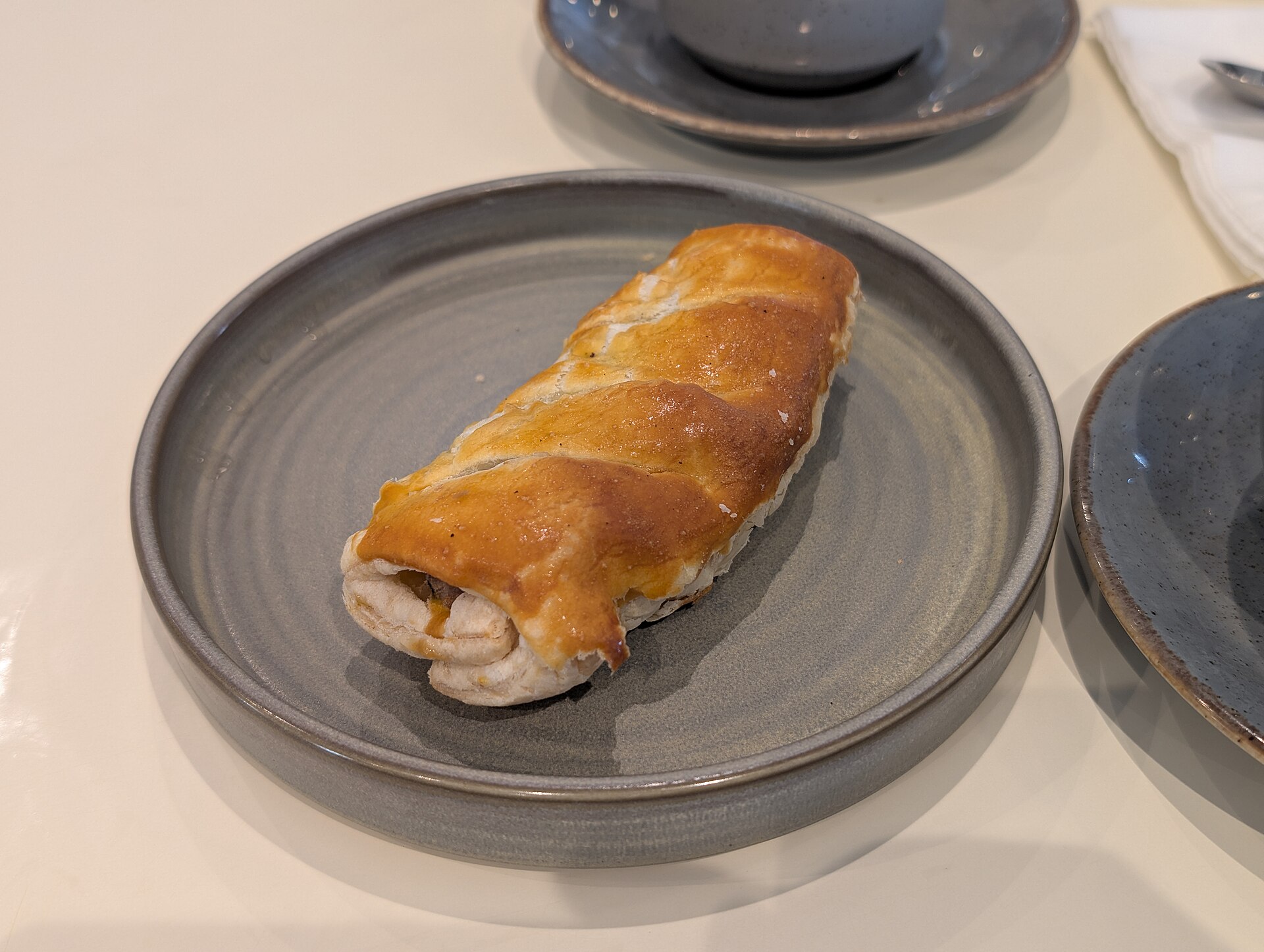 Golden flaky sausage roll on a gray plate, the star of Paul Hollywood party food