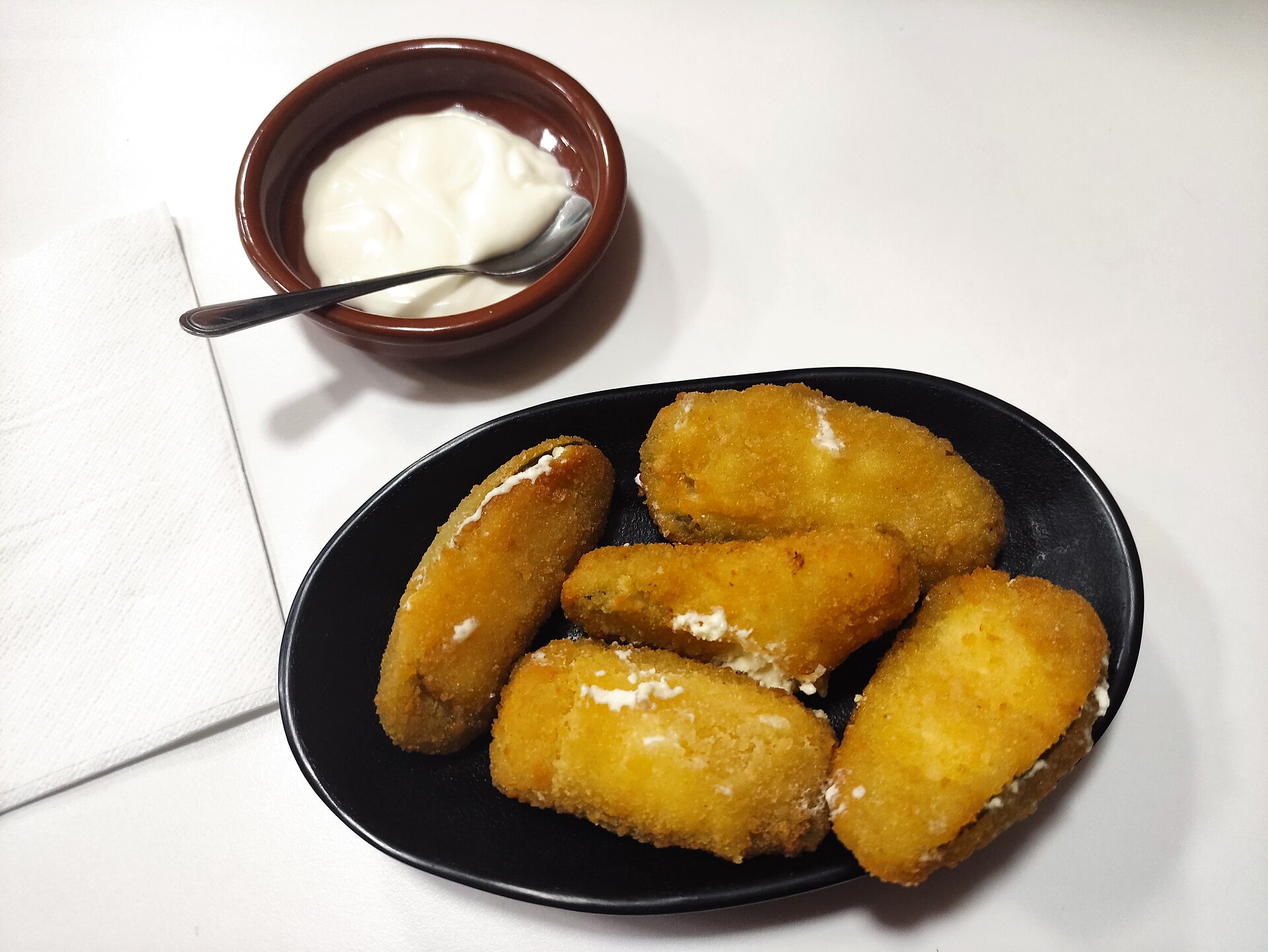 Jalapeno popper recipes: golden breaded poppers in a black bowl with sour cream