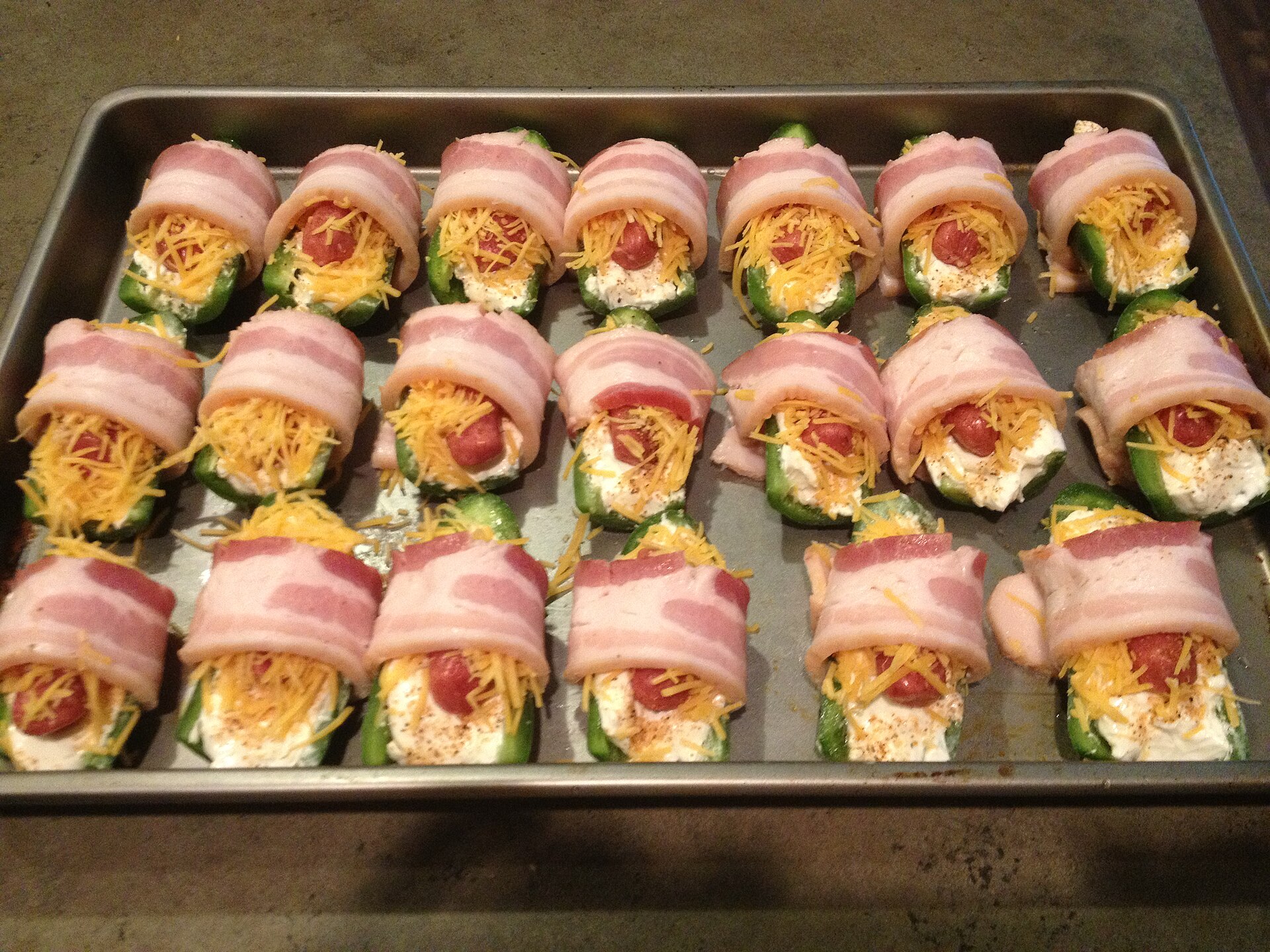 Bacon wrapped jalapeno poppers with cheddar and little smoked sausages on a sheet pan
