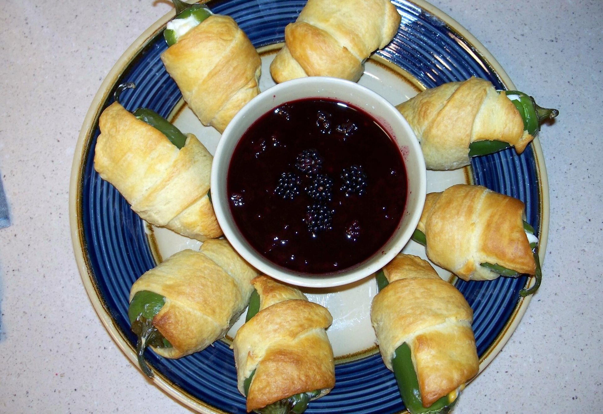 Jalapeno poppers wrapped in crescent dough around a bowl of blackberry dipping sauce