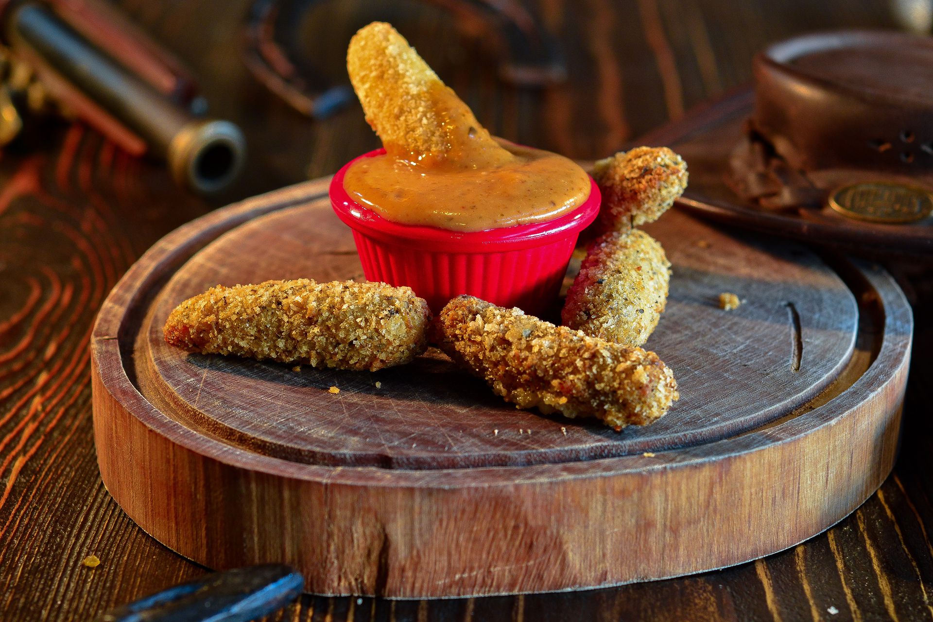 Crispy breaded jalapeno poppers with a dipping sauce on a wooden board