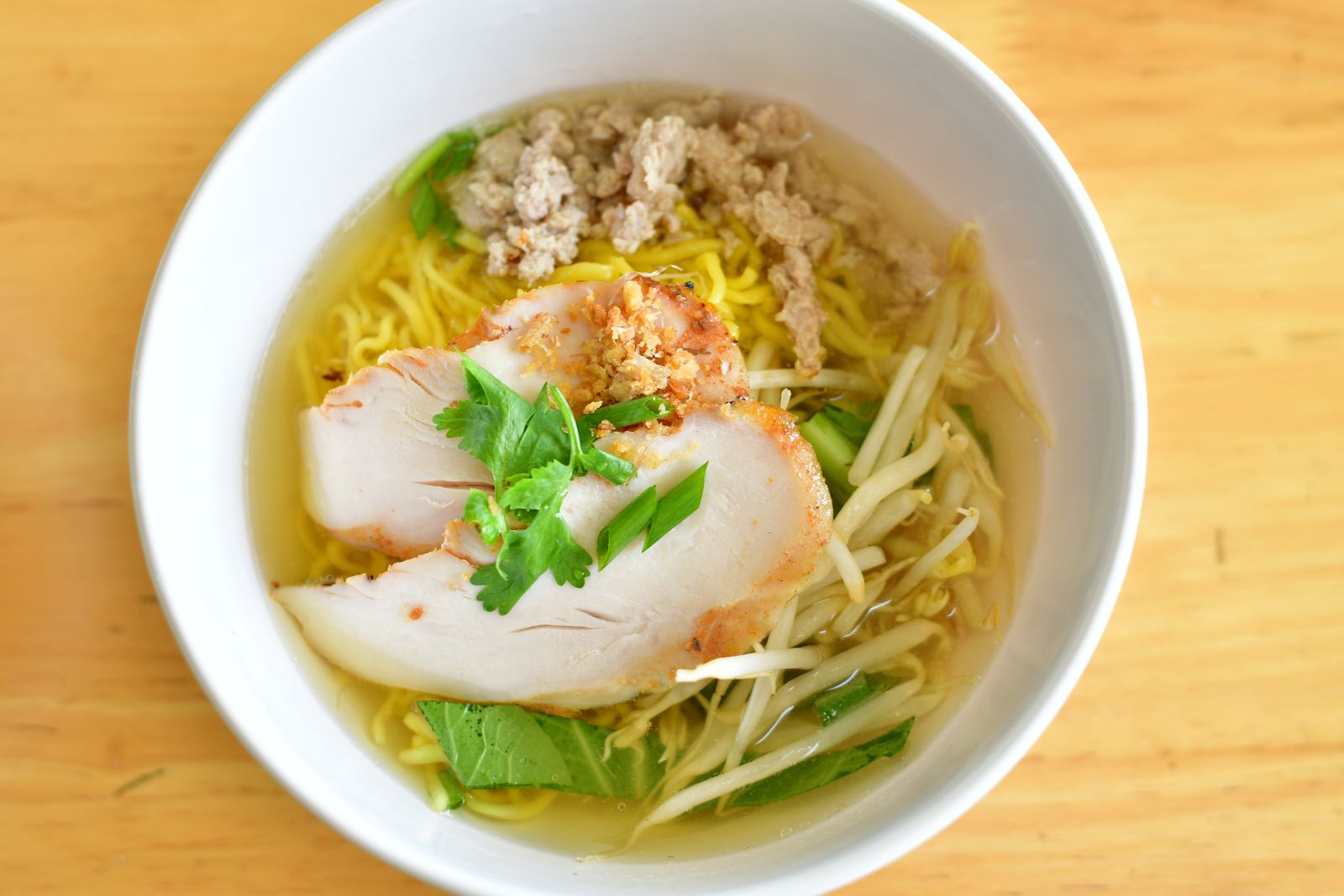 Chicken ramen soup with greens in a white bowl