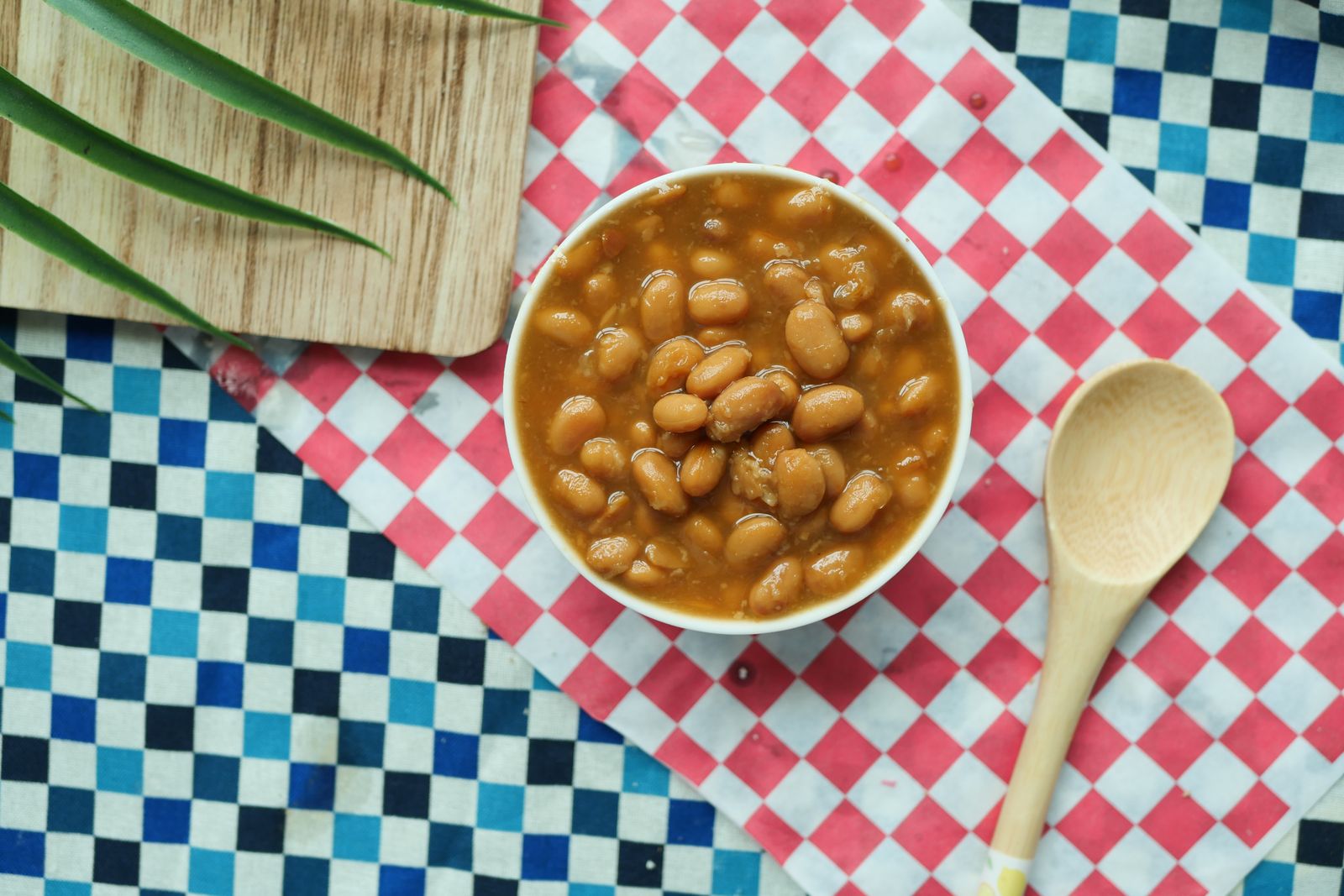 A bowl of saucy beans next to a wooden spoon