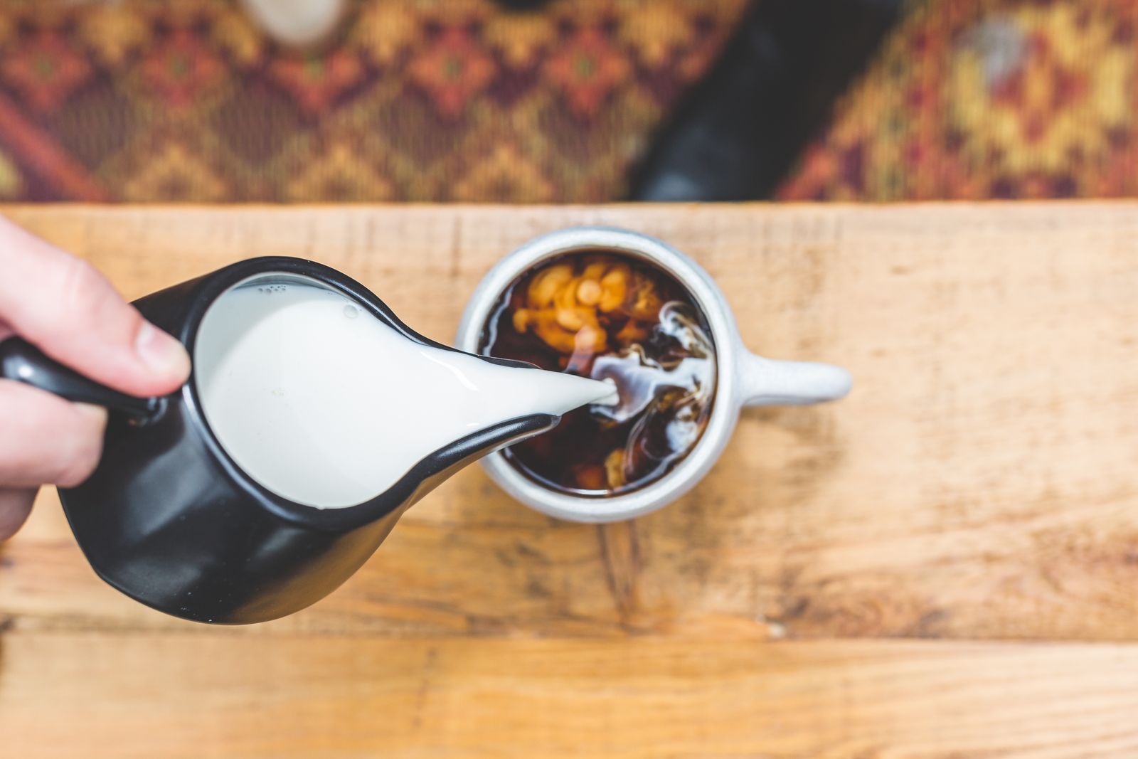 Milk poured from a small jug into a hot cup on a wooden table