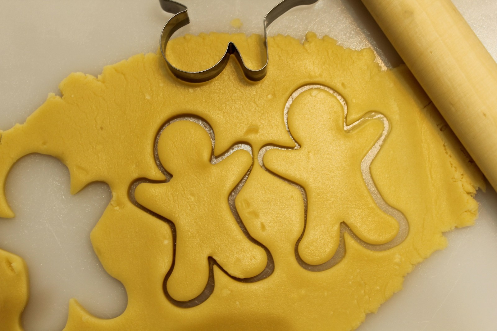 Gingerbread dough being cut with simple metal gingerbread man cookie cutters