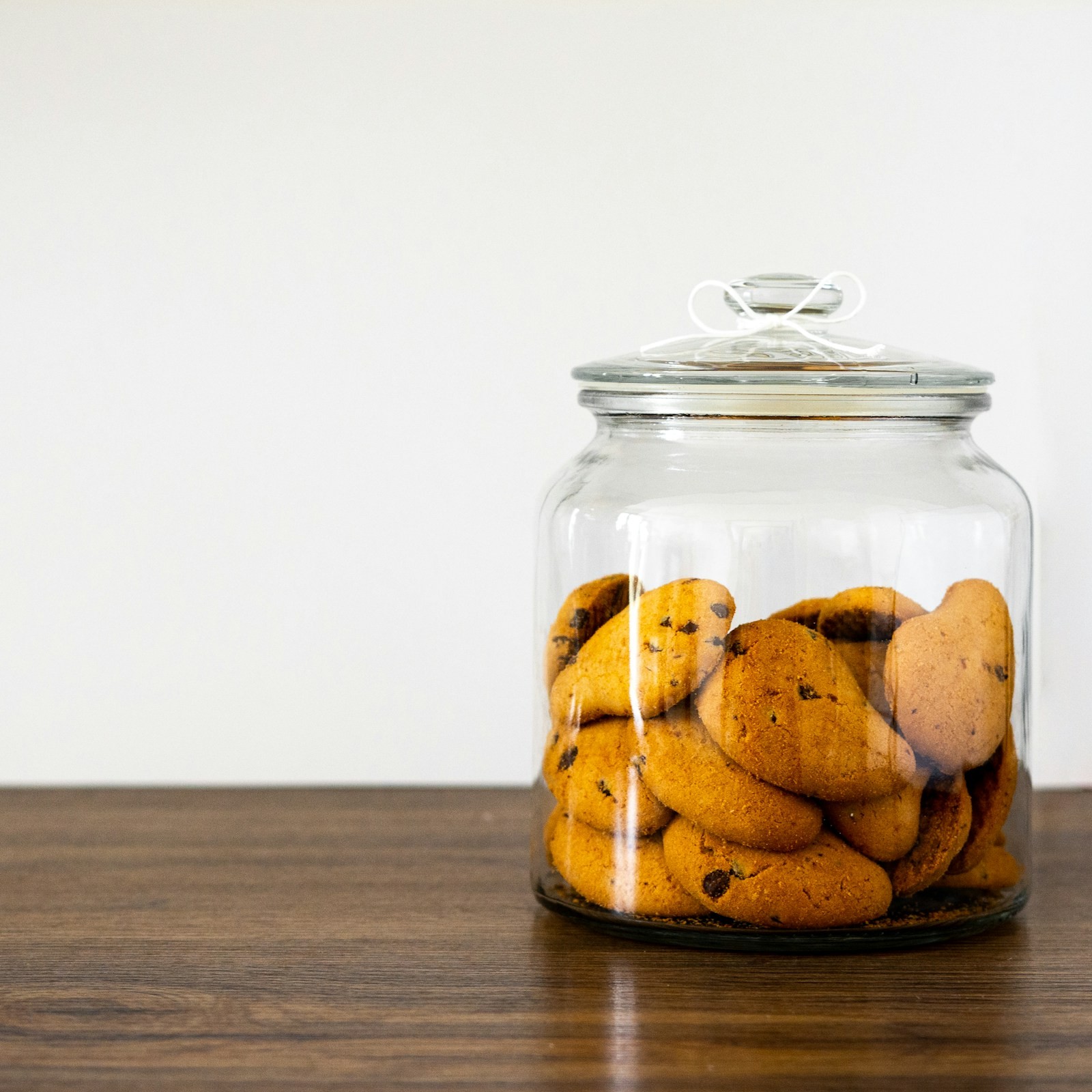 Glass cookie jar filled with crisp cookies on a wooden shelf