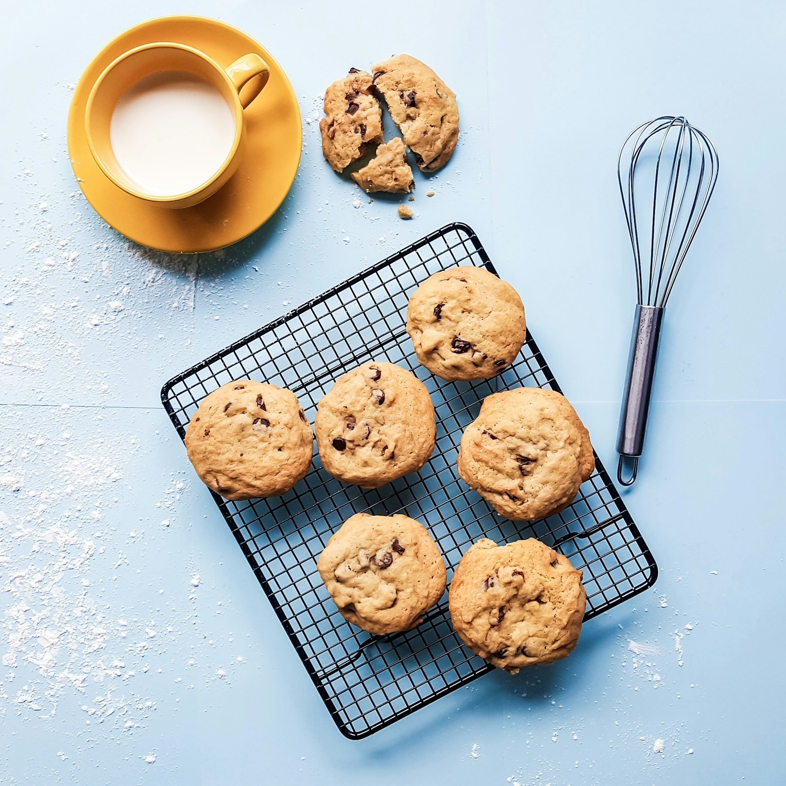 Chocolate chip cookies cooling on a wire rack next to a whisk
