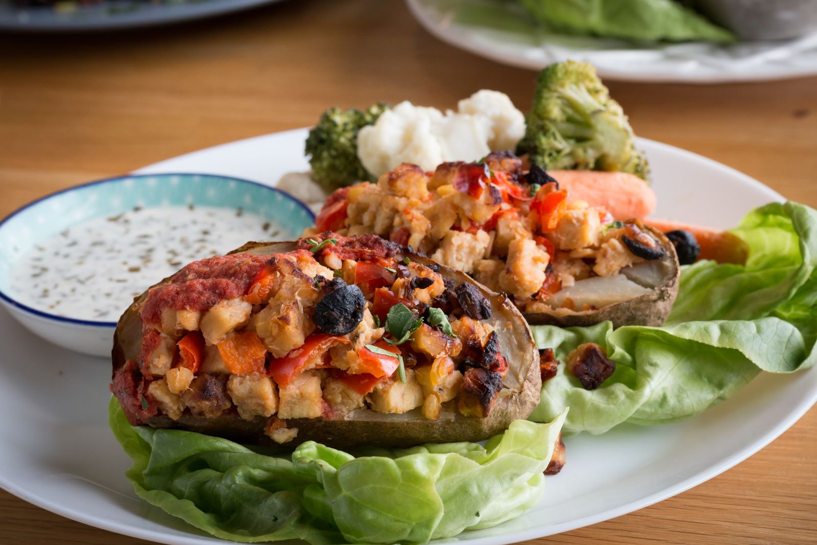 A stuffed baked potato with a creamy sauce on the side