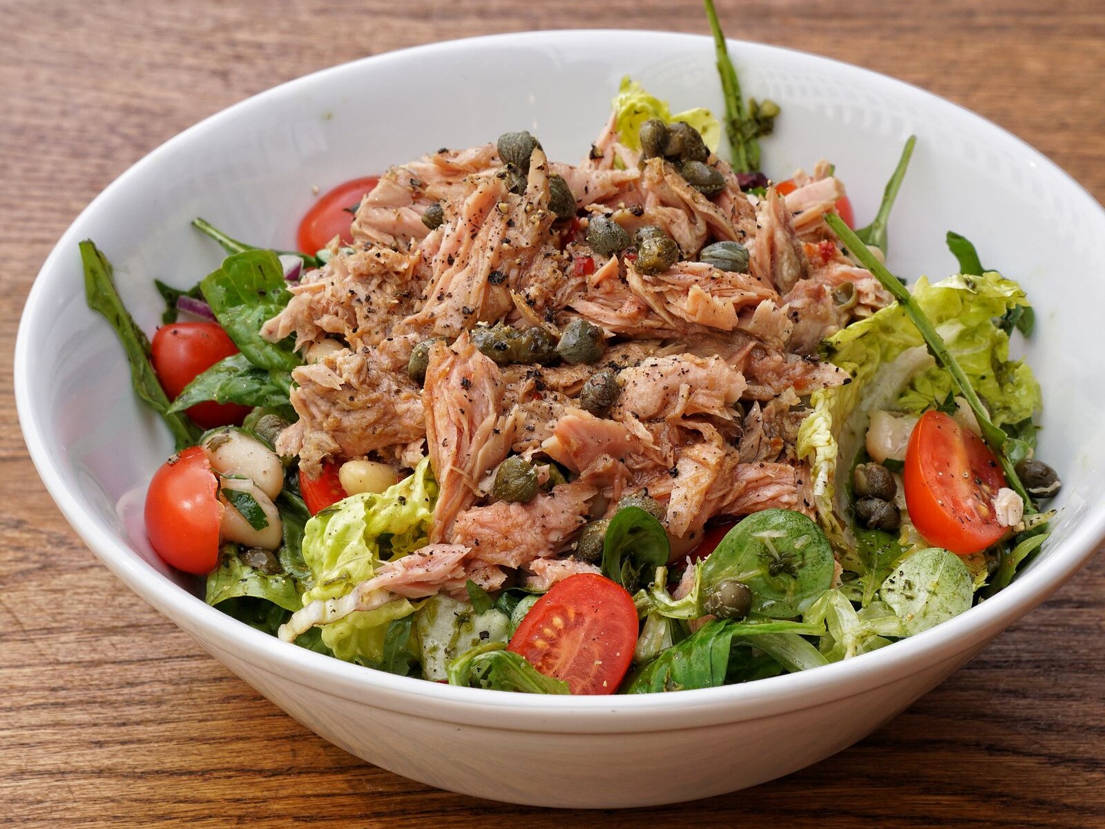 A bowl of tuna salad with tomatoes and greens