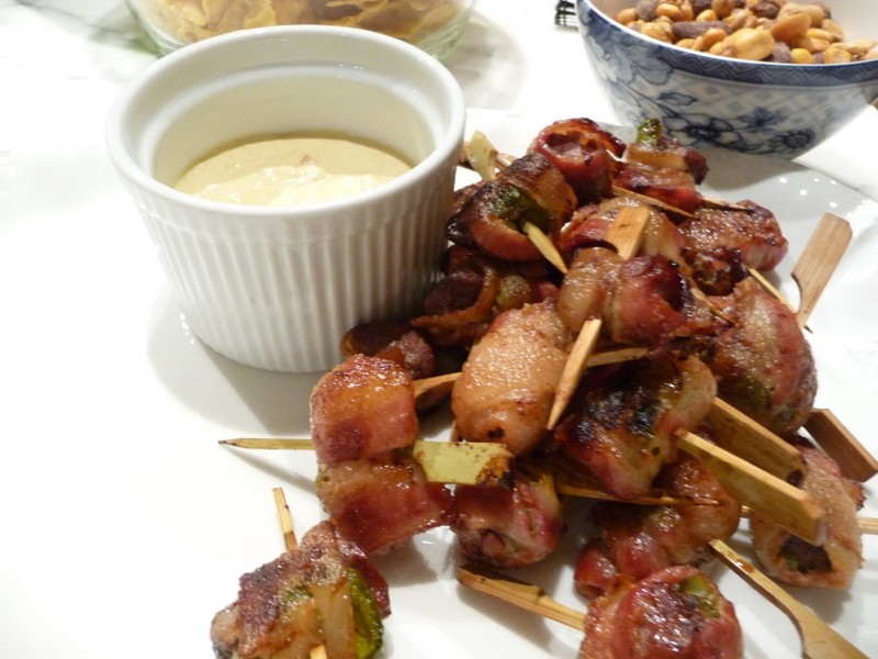 Bacon-wrapped rumaki appetizers on toothpicks with a small dipping sauce