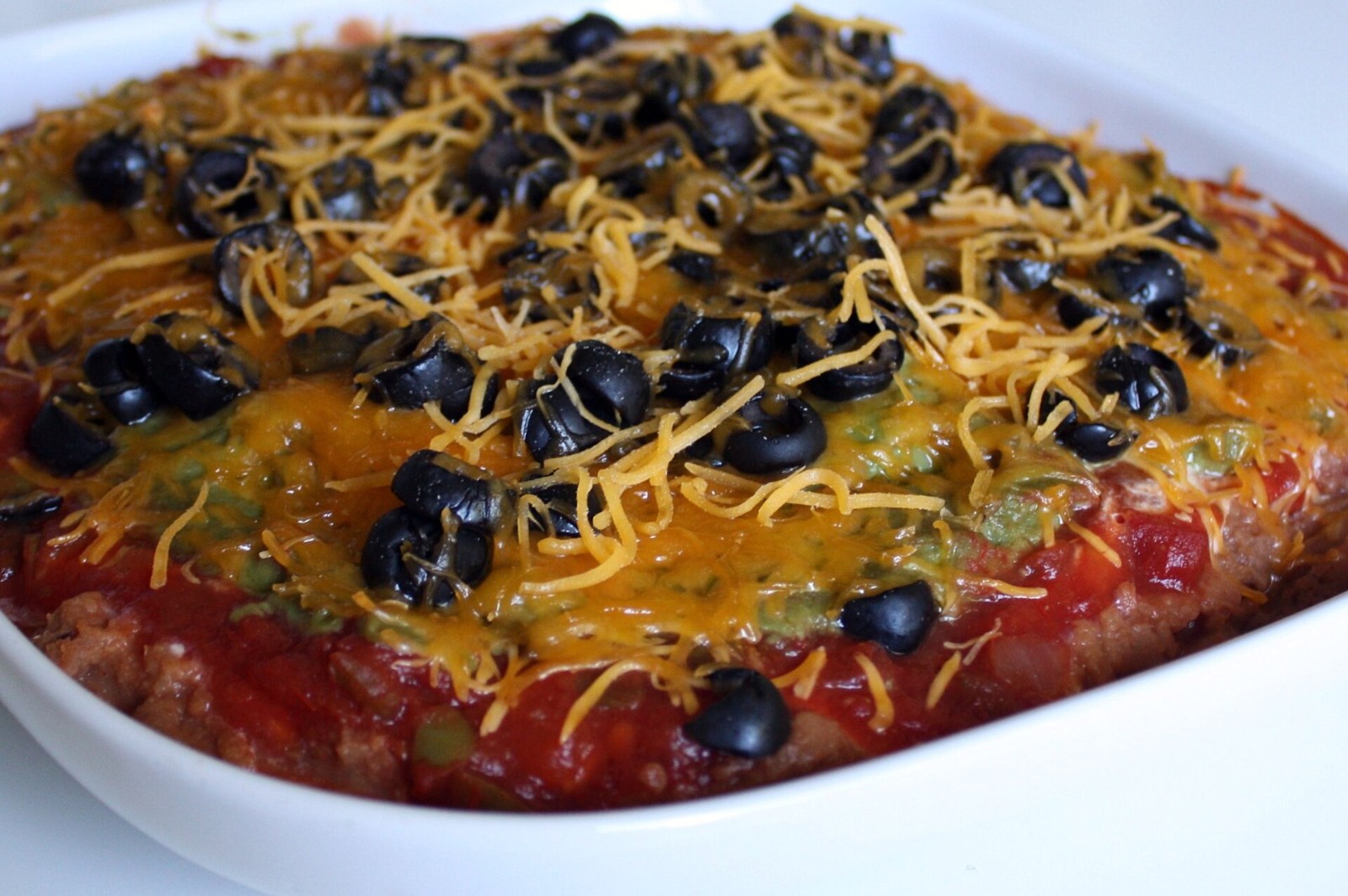 Seven-layer bean dip topped with cheddar and black olives, a grandma party favorite