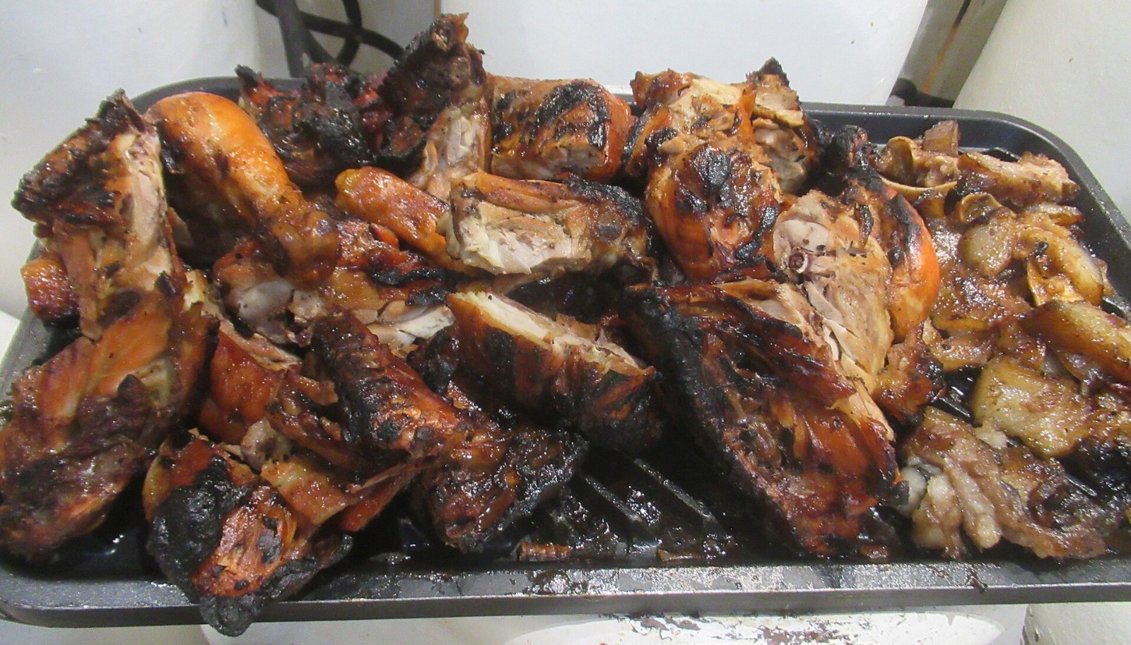 Charred glazed barbecue chicken pieces piled on a tray