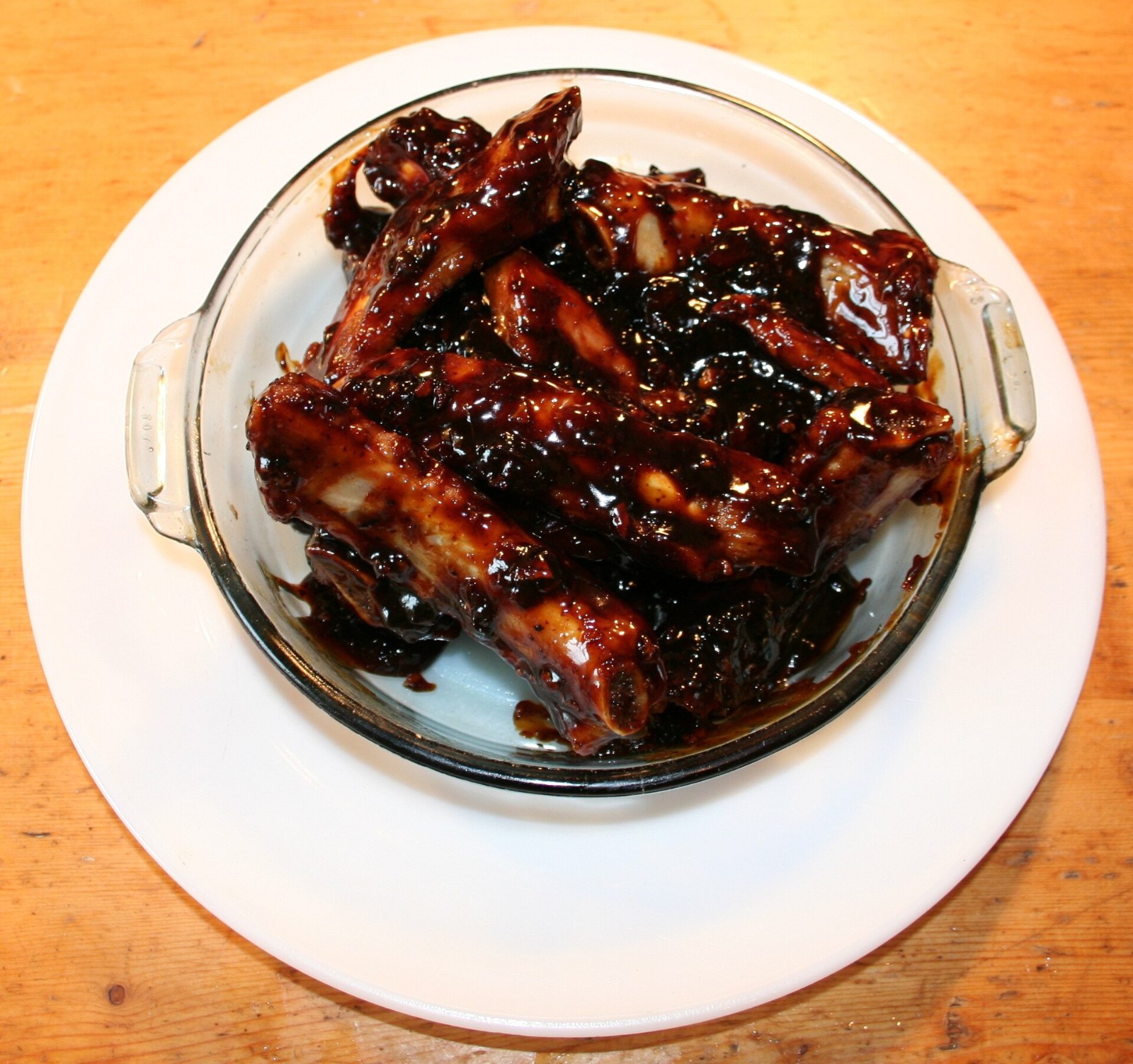 Sticky glazed spare ribs in a glass dish on a white plate