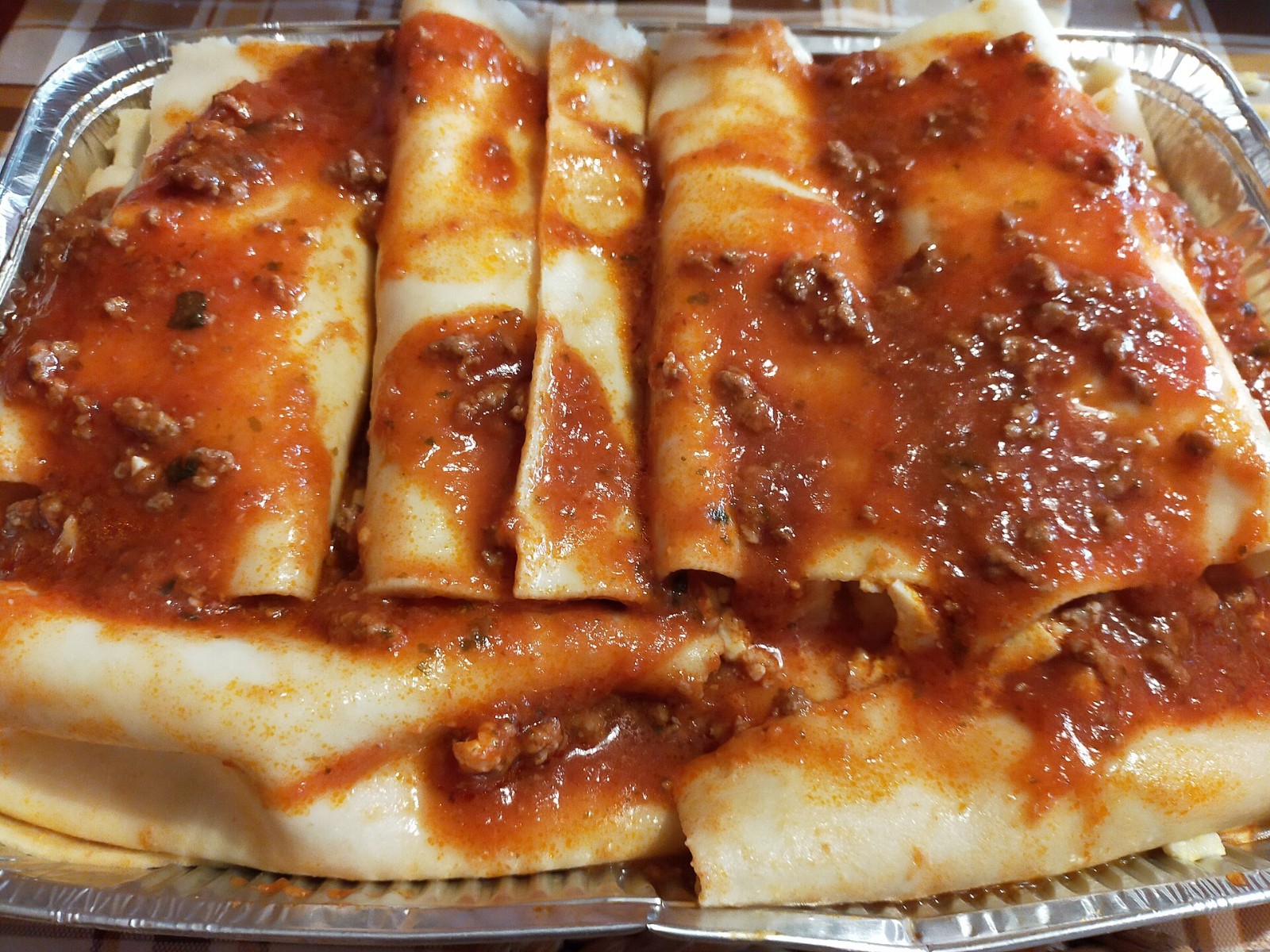 Homemade cannelloni tubes in rich meat ragu in a pan