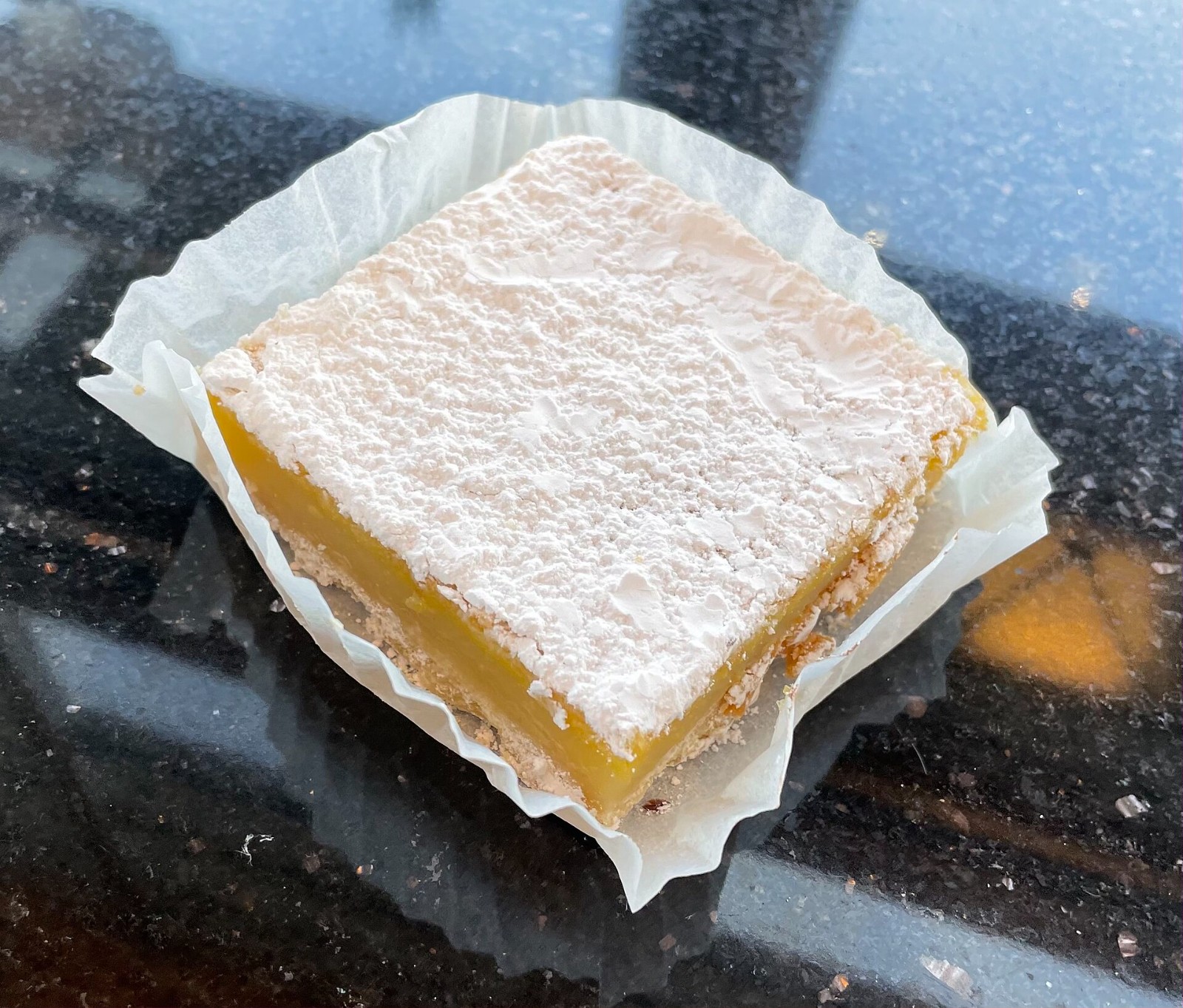 Lemon bar with a powdered sugar top in a paper liner