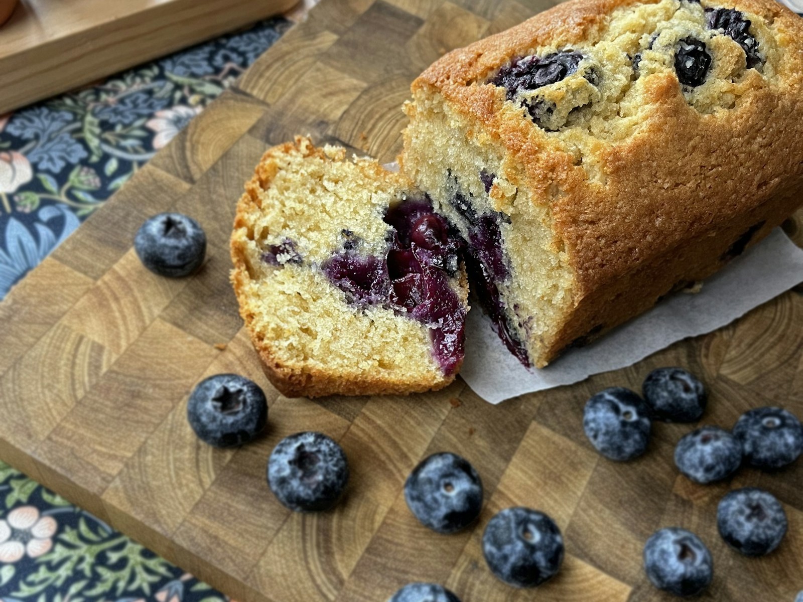Sliced blueberry loaf on a wooden board with fresh blueberries scattered around