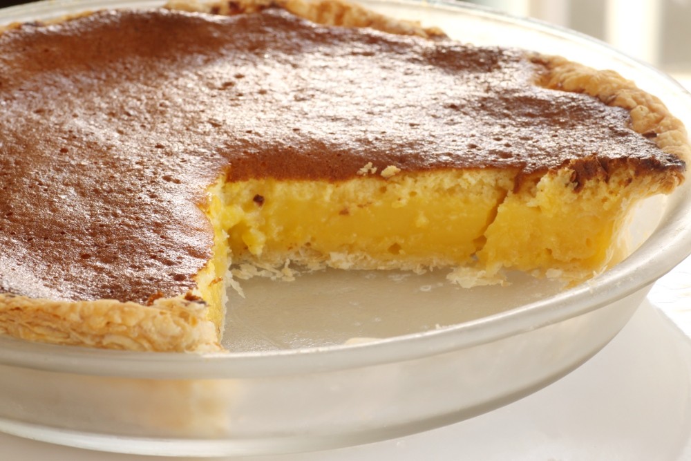 Southern chess pie with a golden sugary top and one slice removed in a glass dish
