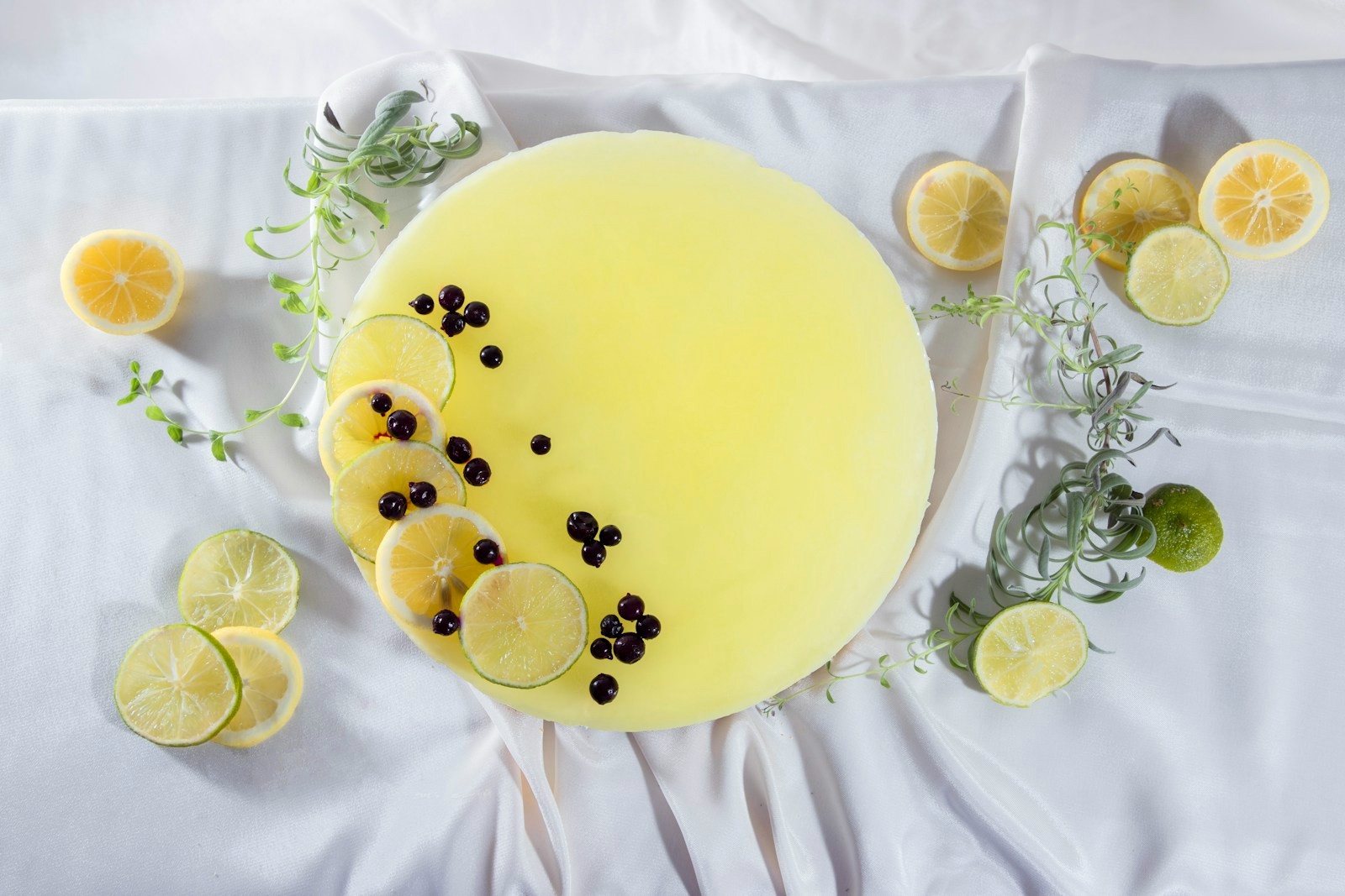 Whole yellow-topped cheesecake decorated with blueberries and citrus slices on white linen