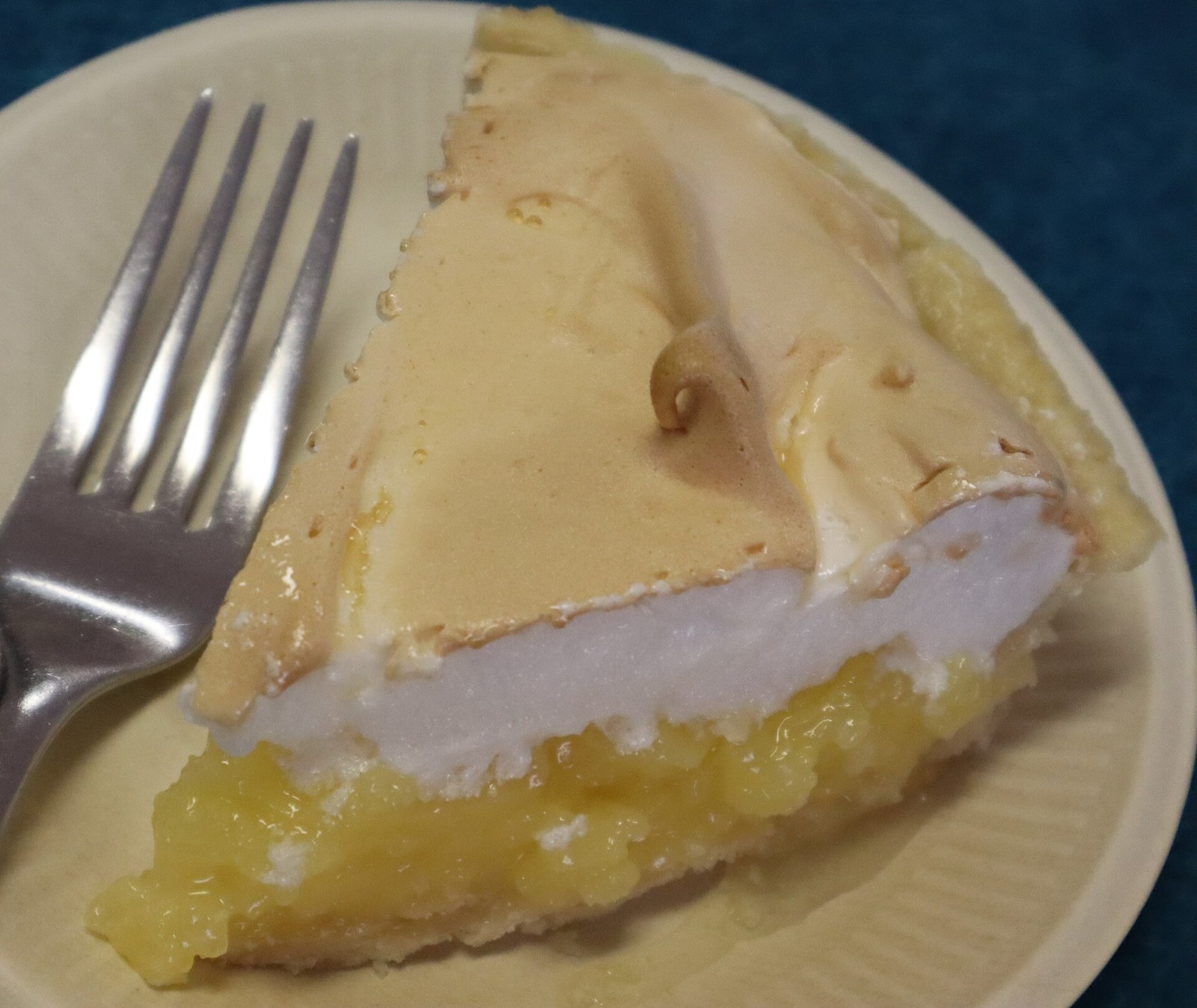 Slice of lemon meringue pie with a tall toasted meringue on a cream plate