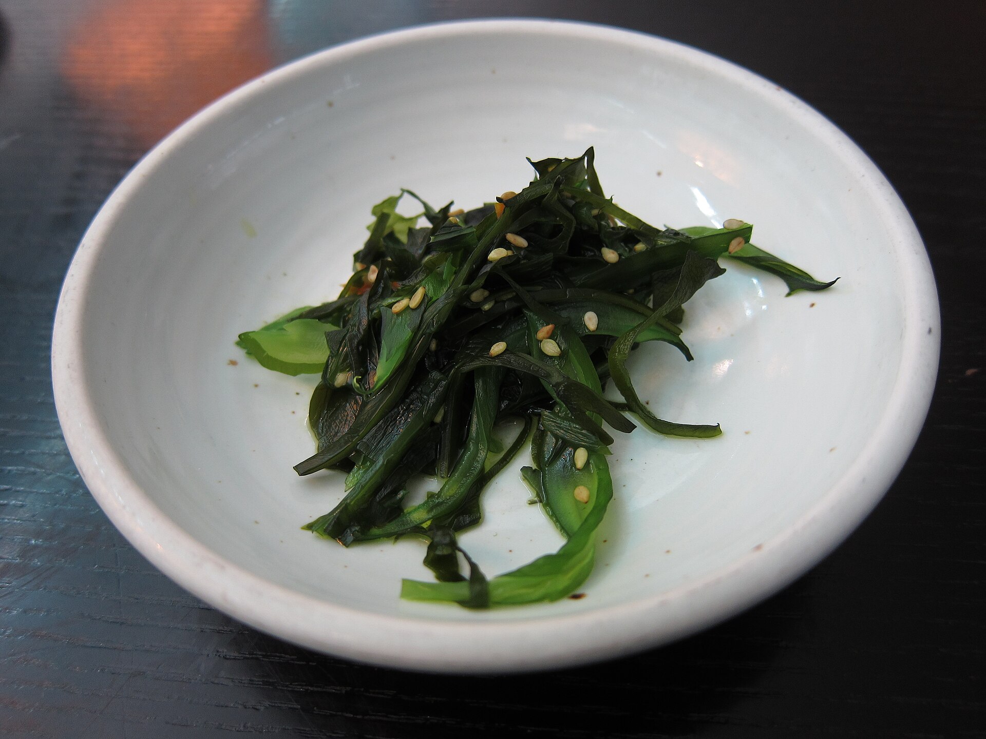 A small white bowl of dark green seaweed salad