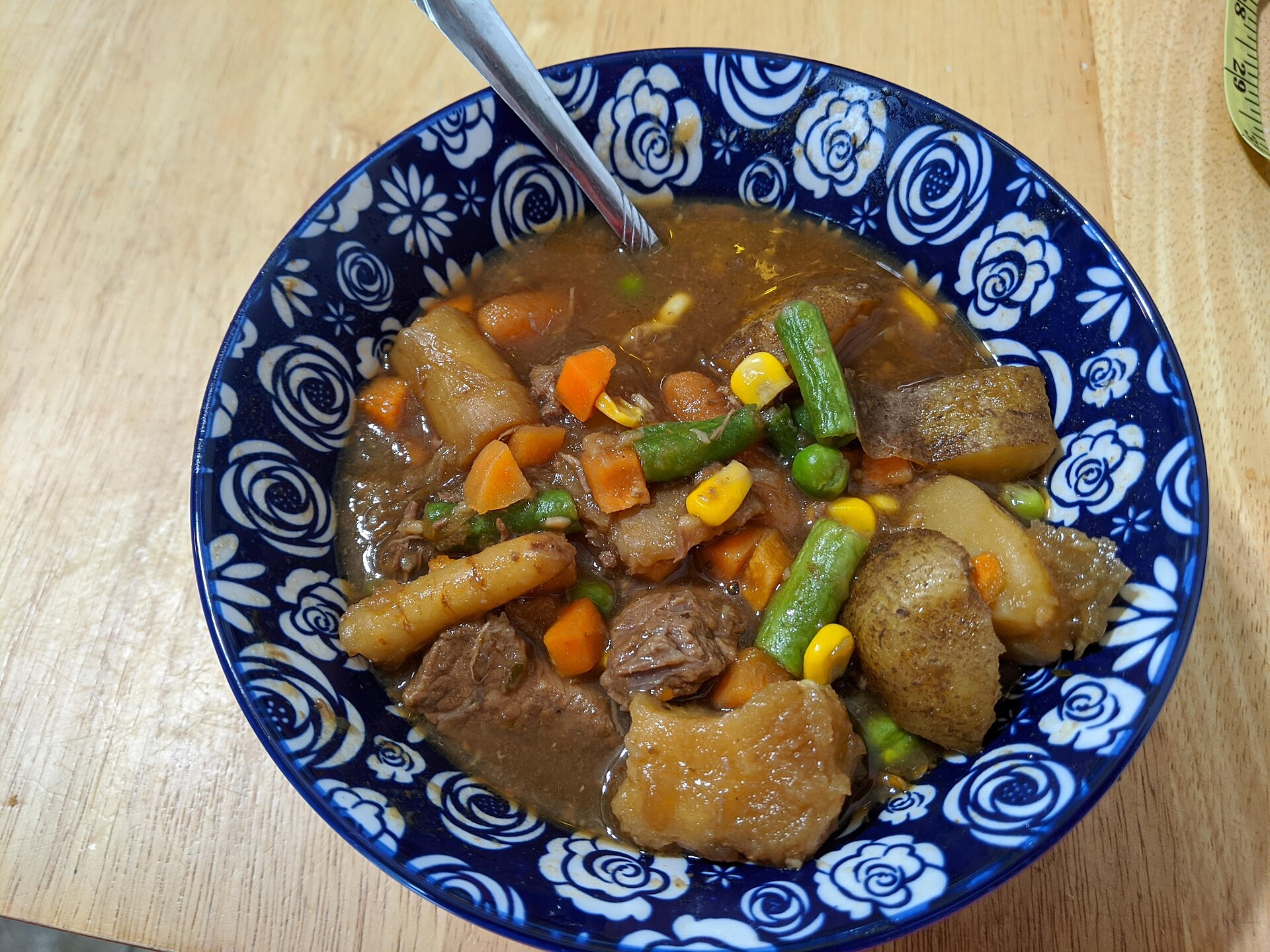 A blue bowl of beef stew with potatoes, carrots and peas