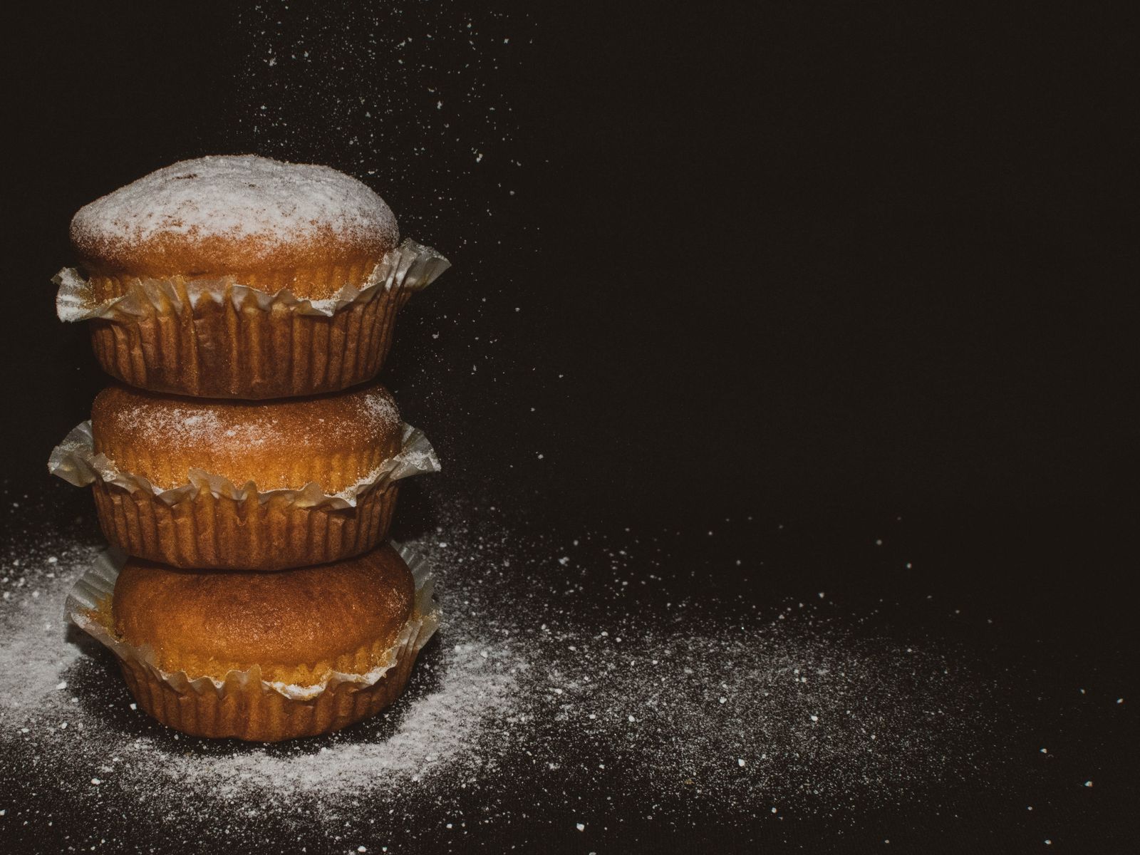 Stacked pumpkin muffins dusted with sugar on a dark table