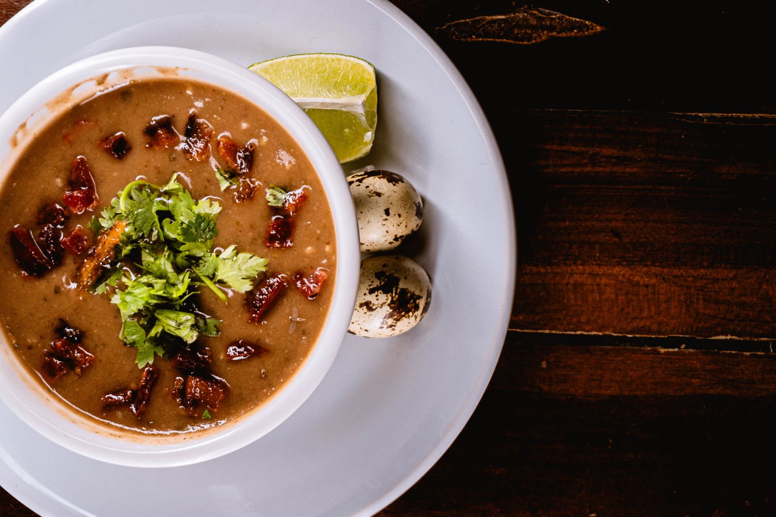 A dark bowl topped with herbs, quail eggs and lime