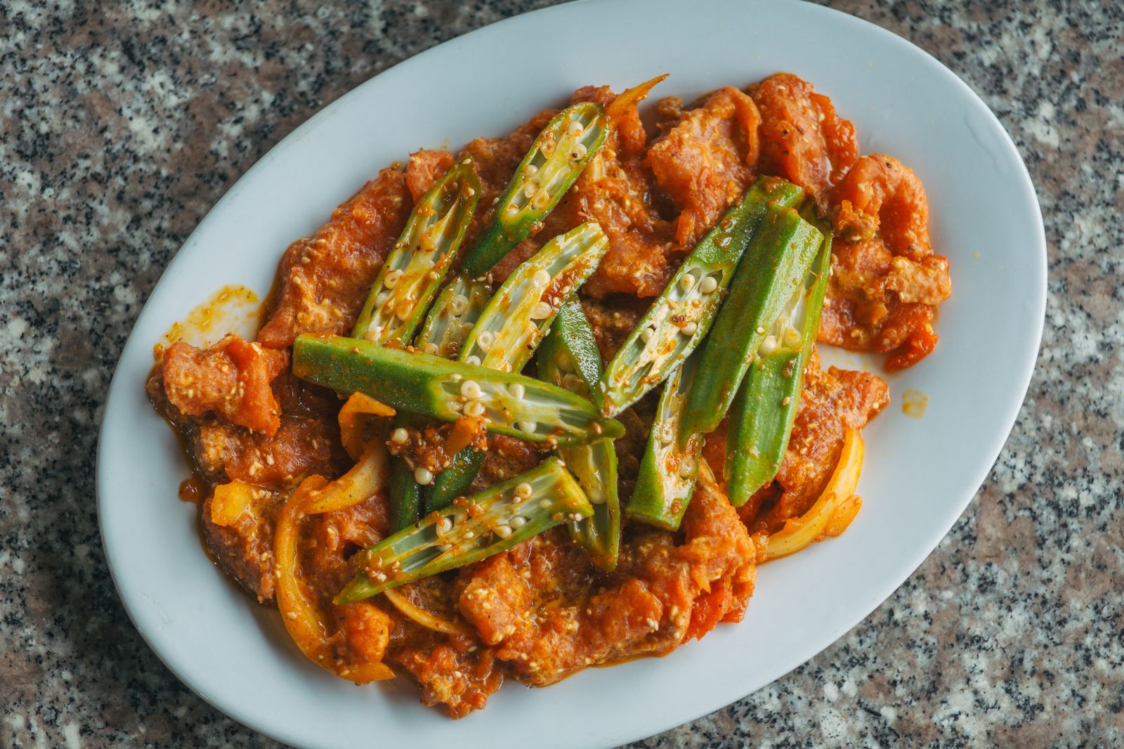Okra smothered with tomatoes and chicken on a white platter