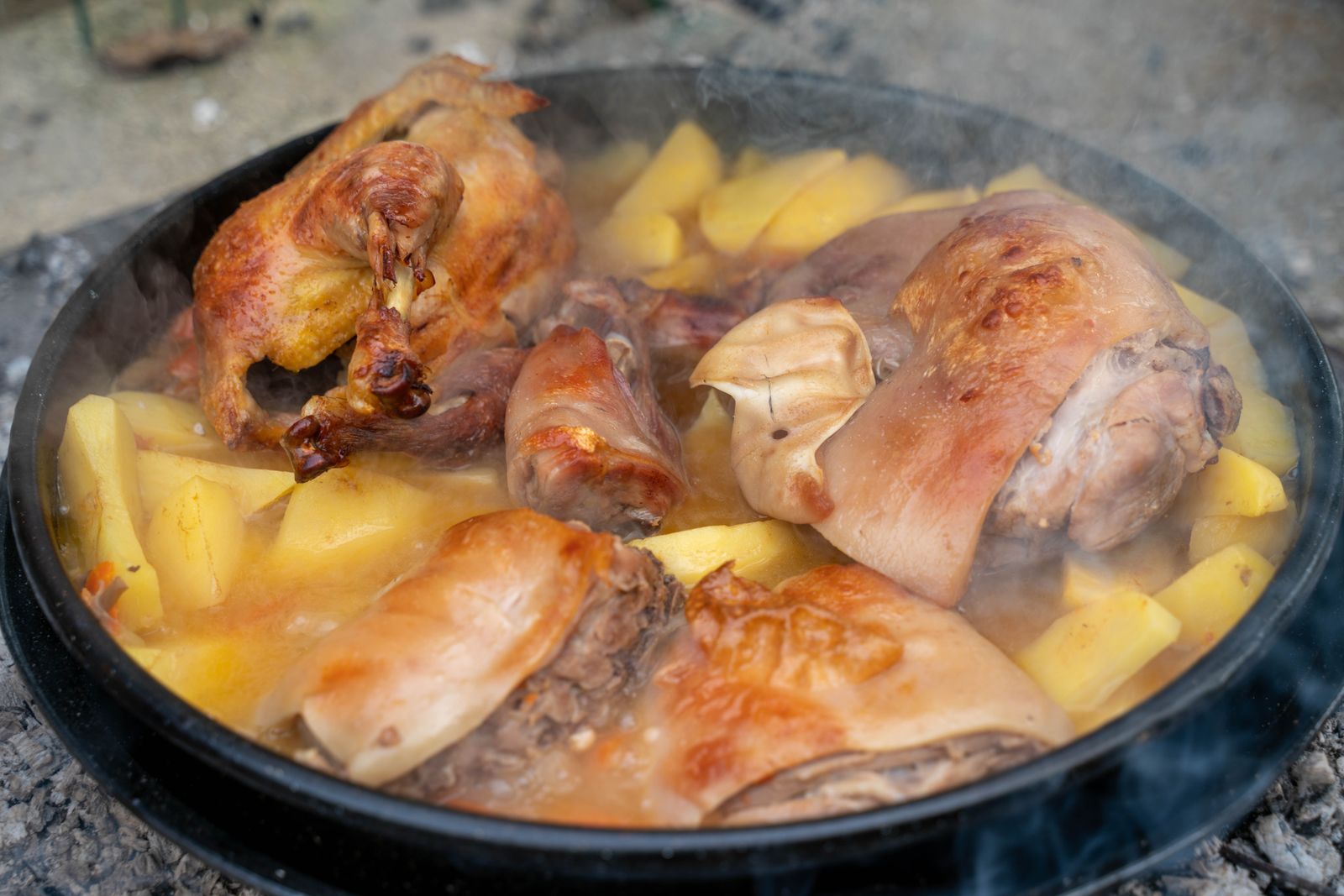 Smothered chicken thighs simmering with potatoes in a black pan