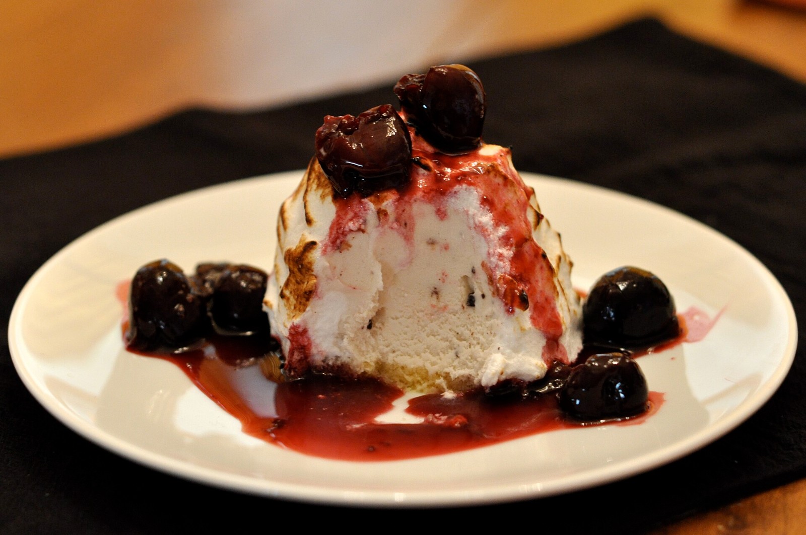 Baked Alaska with toasted meringue and dark cherries on a white plate