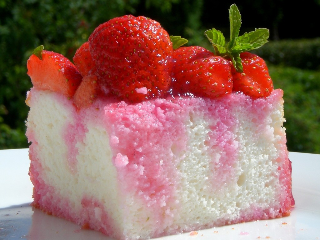 Slice of retro strawberry poke cake dessert with pink streaks and fresh strawberries on top