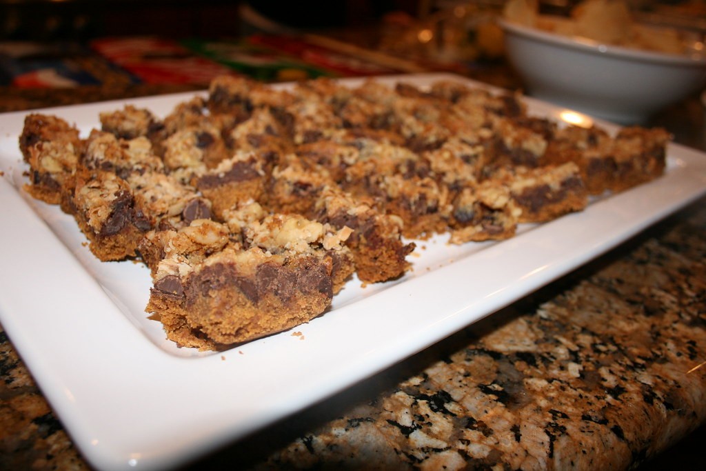 Squares of 1970s seven-layer bars with coconut, chocolate chips and nuts on a white platter