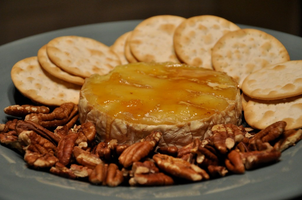 Brie topped with honey and pecans surrounded by crackers