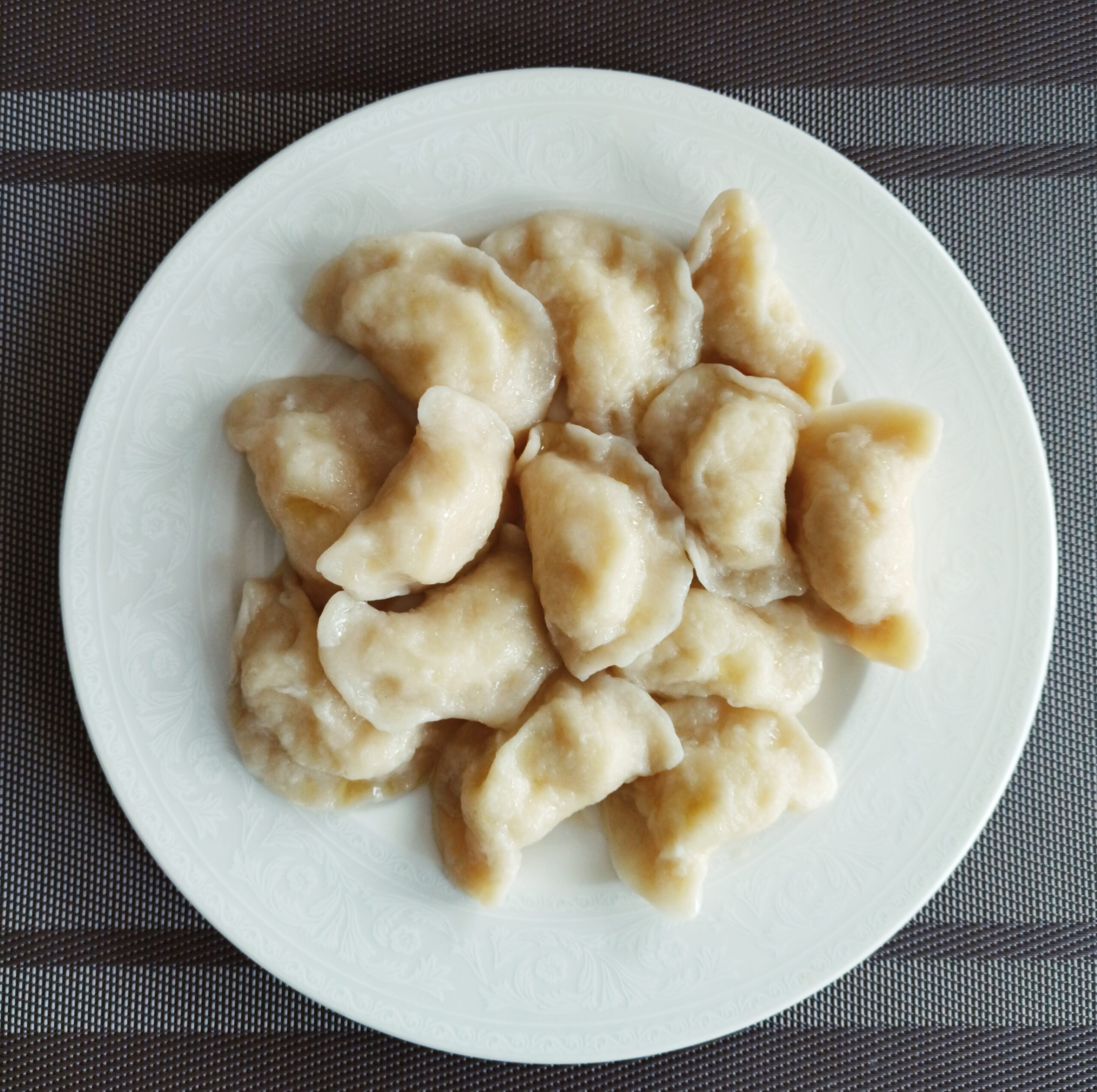 Potato pierogi with melted butter on a white plate