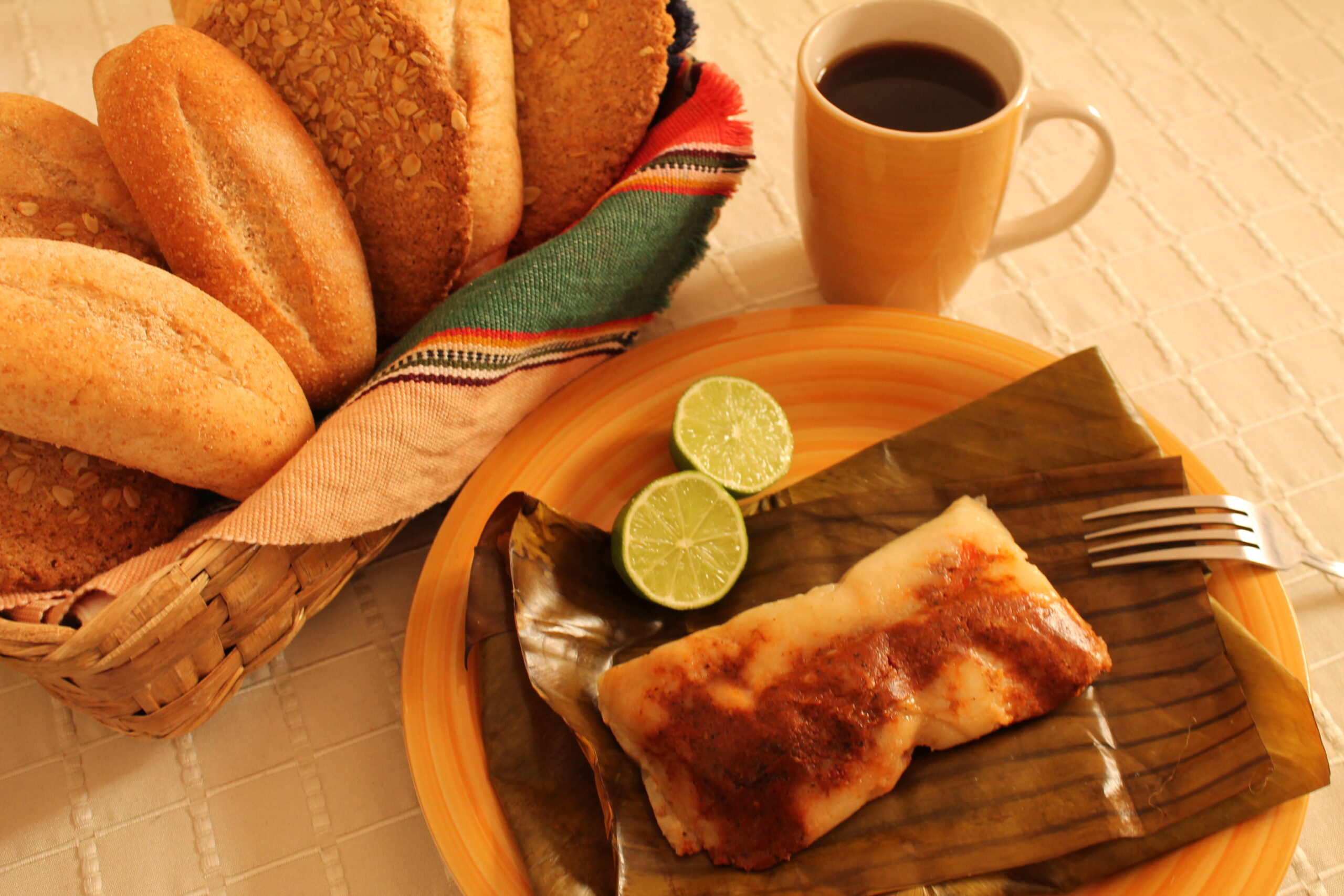 Guatemalan tamal colorado in a banana leaf with bread rolls and coffee