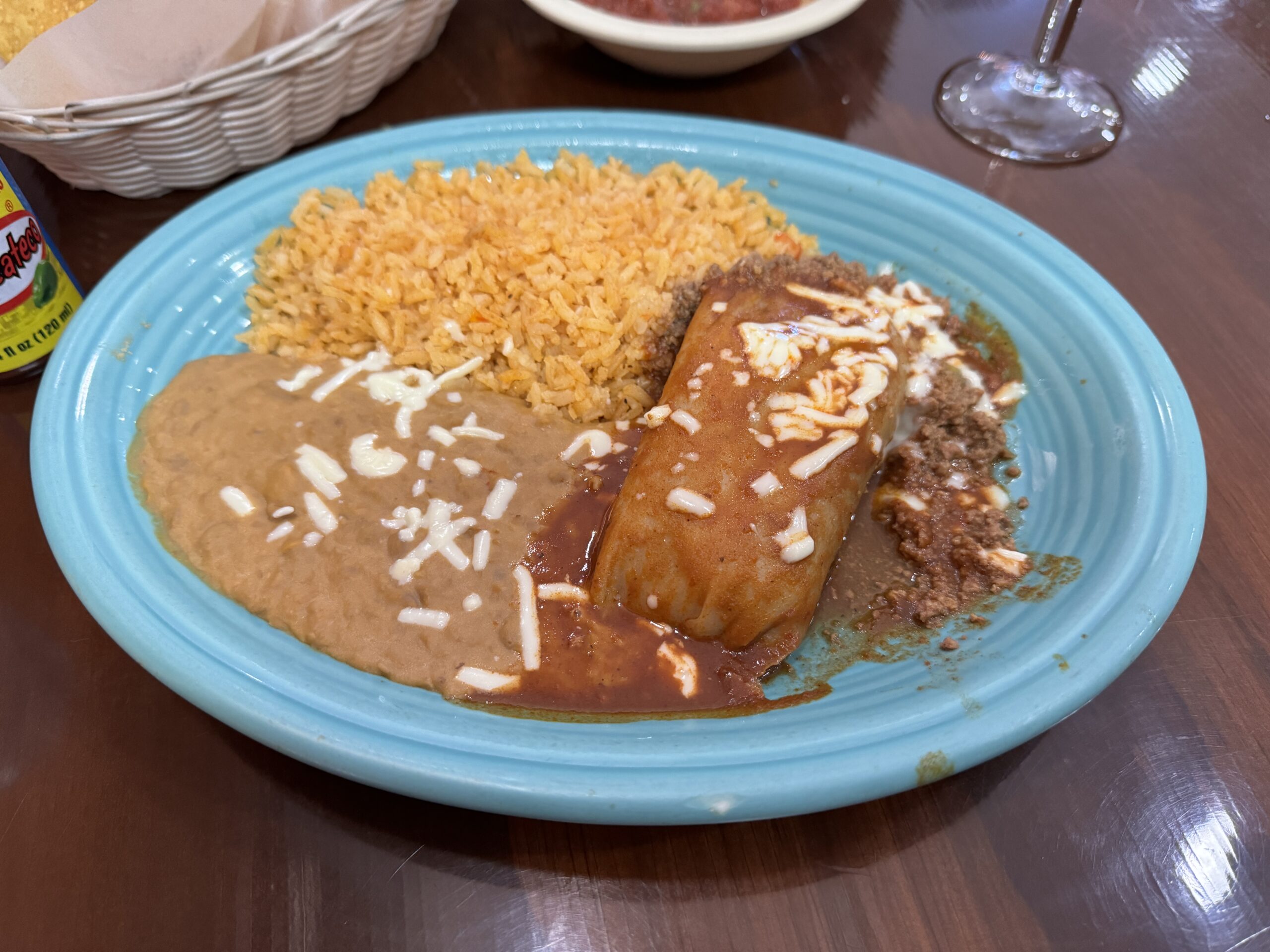 Pork tamale topped with red chili sauce and ground beef with rice and refried beans