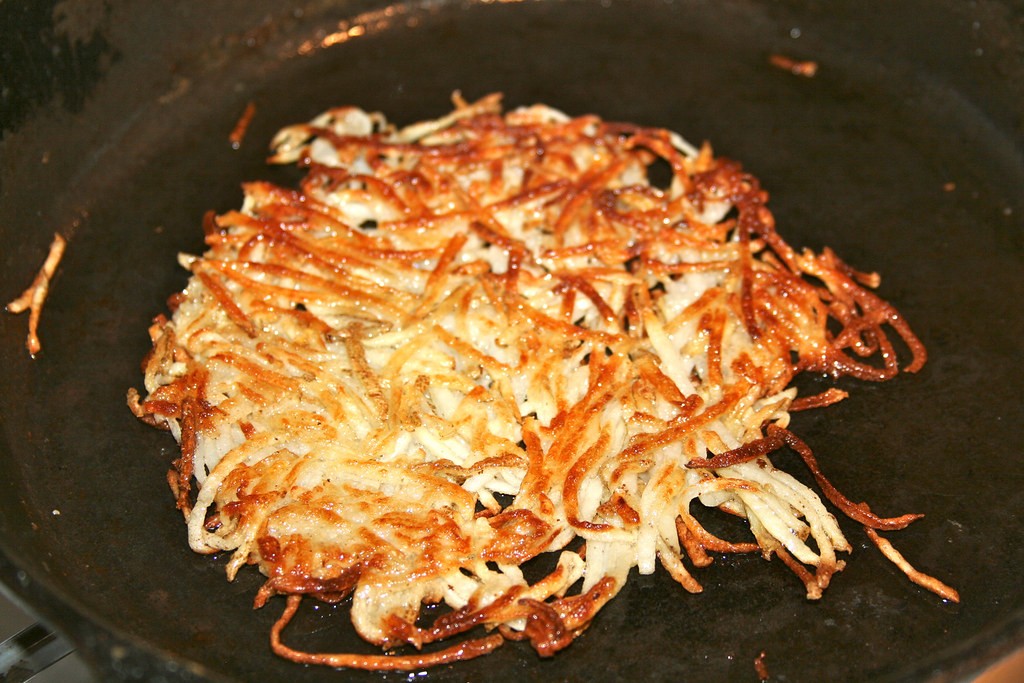 Lacy golden potato shreds sizzling in a black skillet