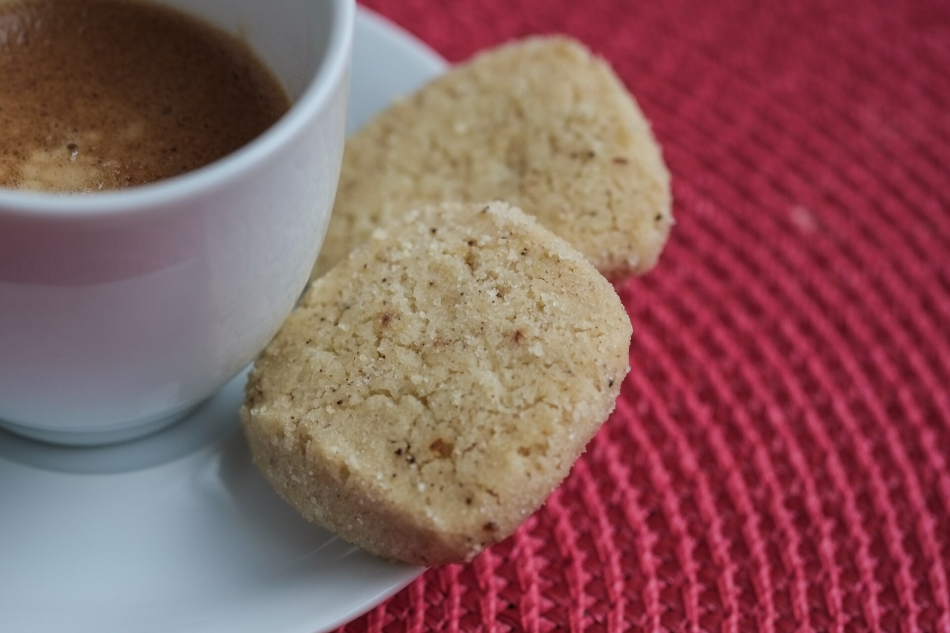 Two sugar-edged German butter cookies on a saucer beside a cup of coffee