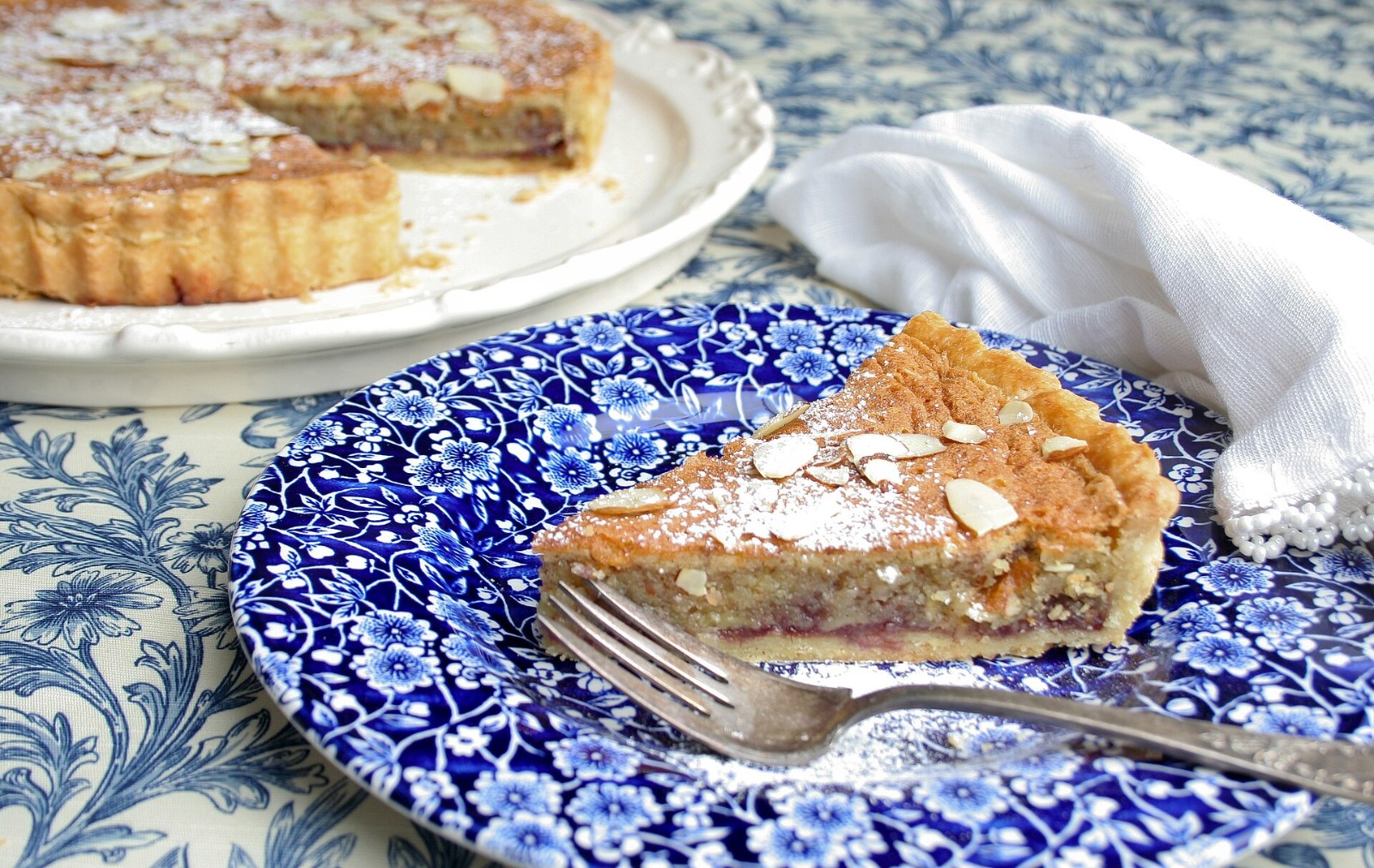 Bakewell tart slice with flaked almonds on a blue plate