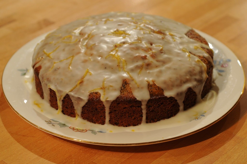 Round lemon drizzle cake with white glaze on a floral plate