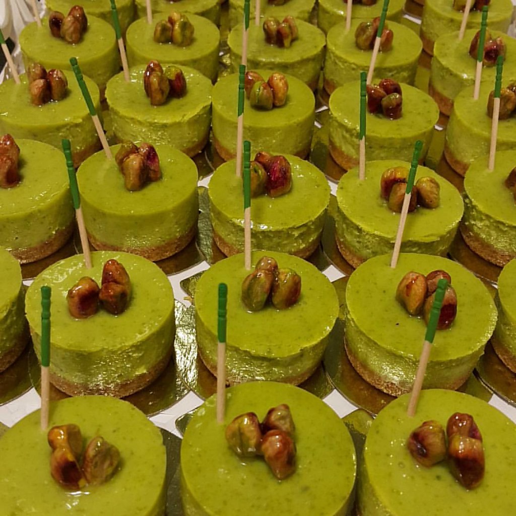 Rows of small green cheesecakes topped with whole nuts on a display tray